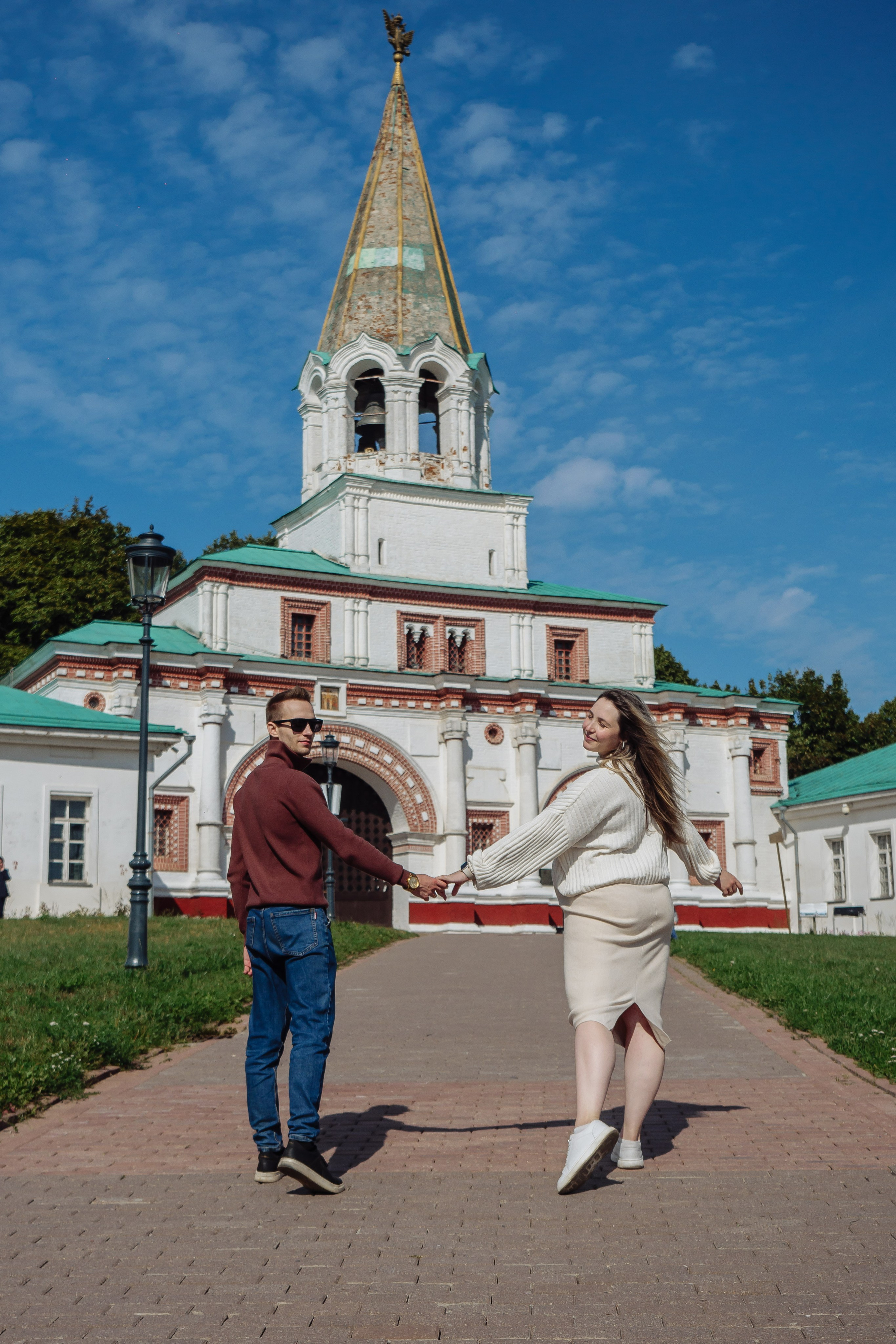 Муж и беременная жена взялись за руки на семейной фотосессии и стоят общим планом на фоне Полковничьи палаты парка -музея Коломенское. Куда сходить в Москве с фотографом: https://foto-video-svadba.ru/kuda-shodit-v-moskve 