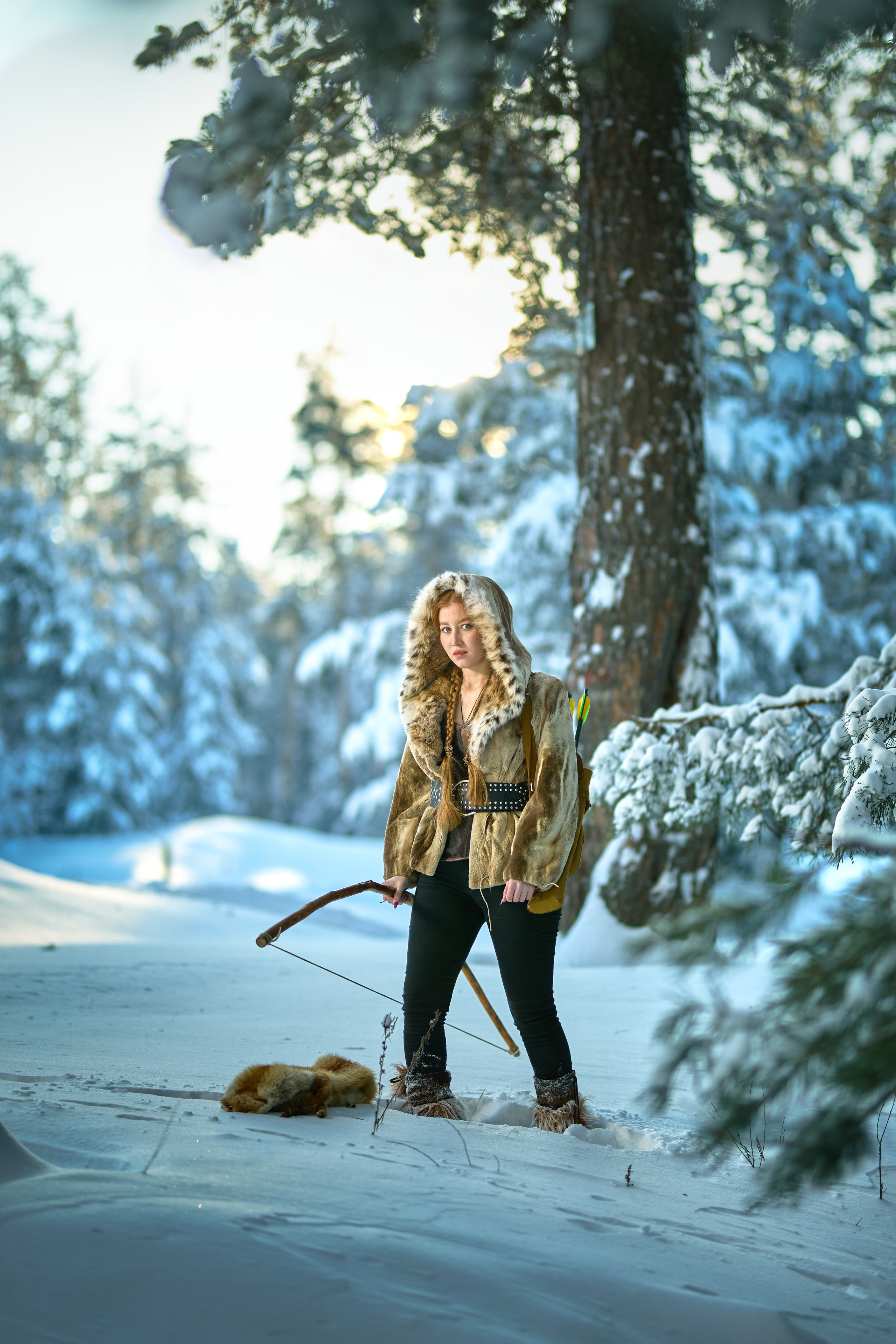 Охотница одетая в меха с луком в руках идет по зимнему лесу