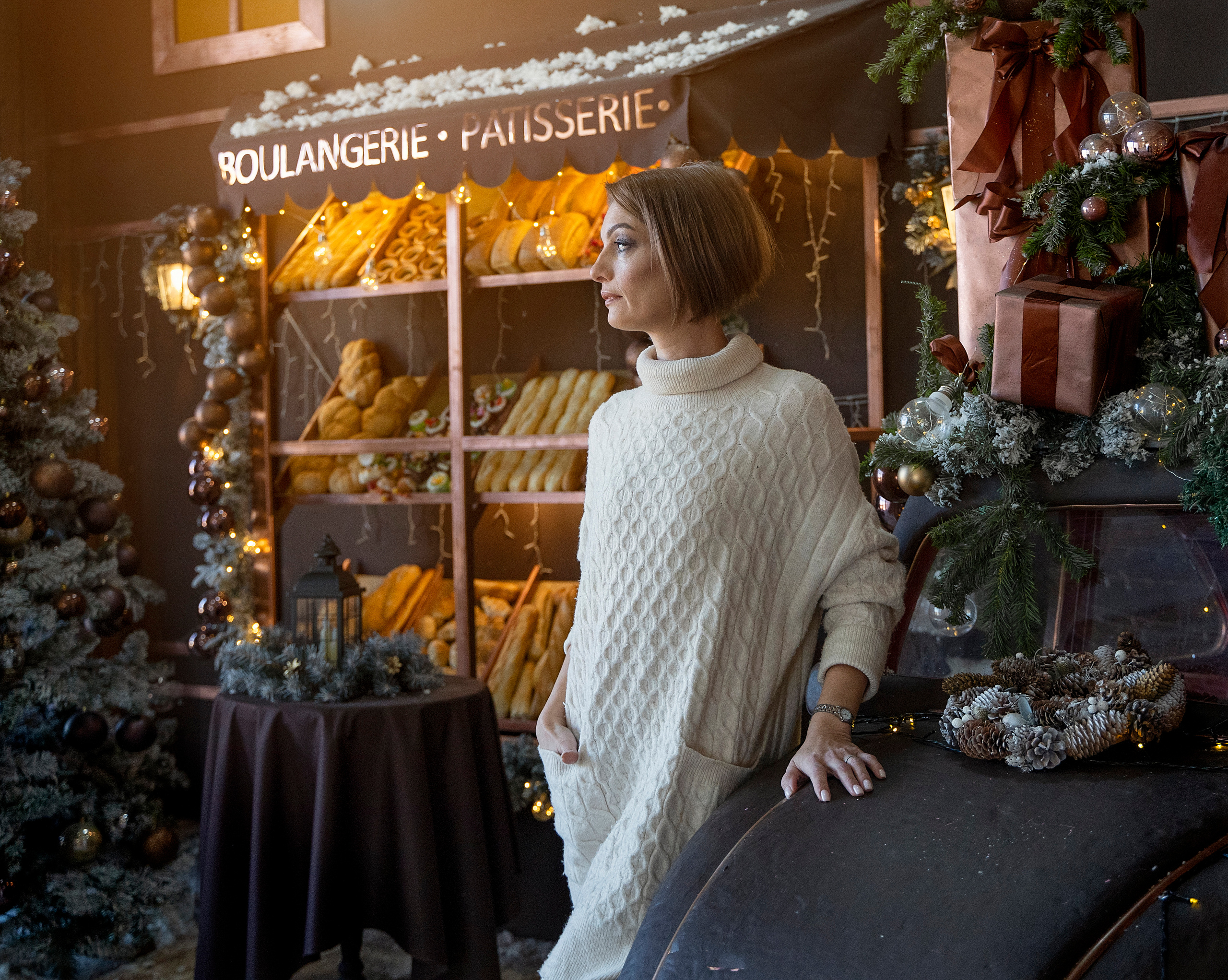 Девушка присела на капот авто, смотрит в даль. На заднем плане витрина хлебного магазина.