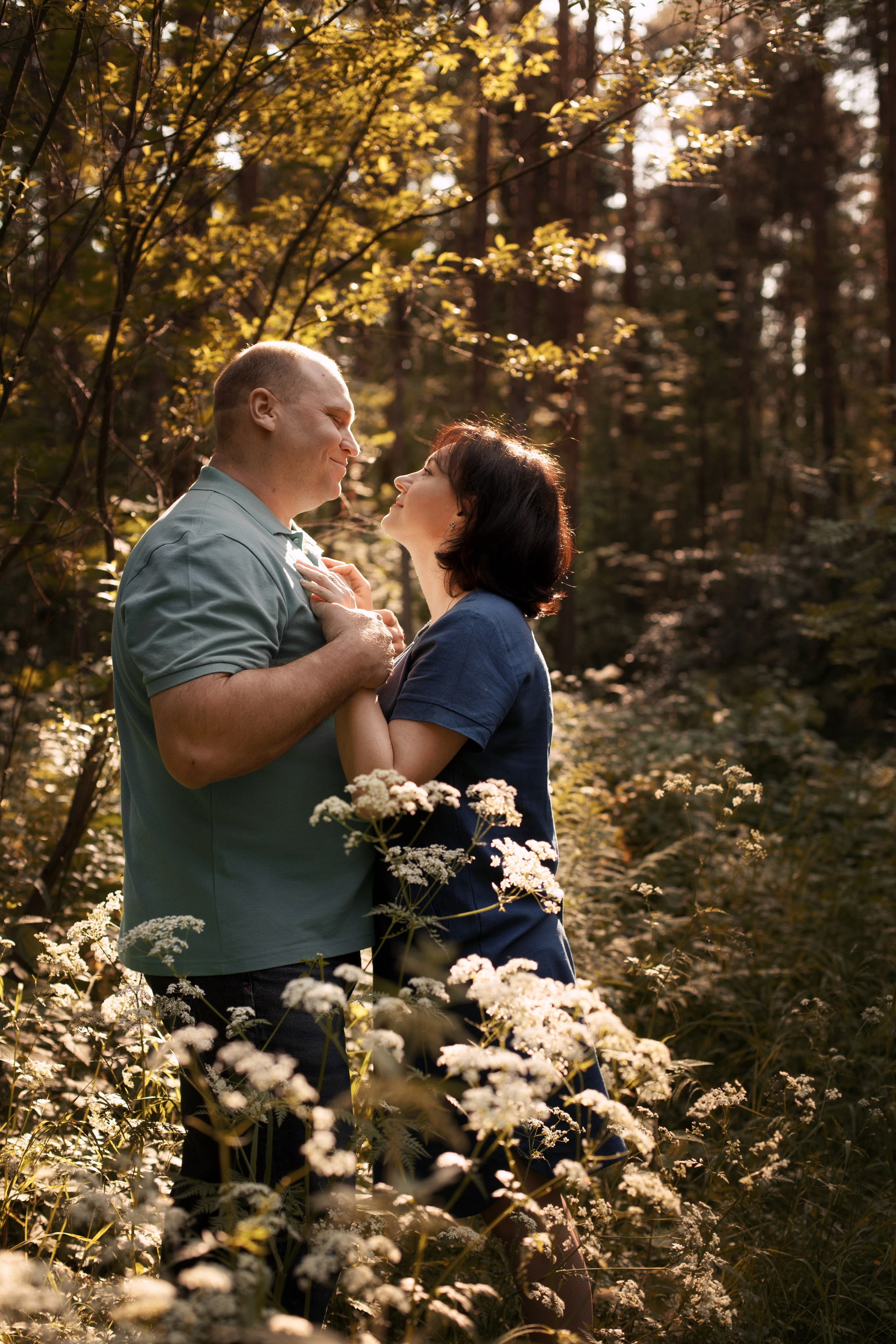 Мужчина и женщина обнимаются в летнем лесу среди полевых цветов в контровом свете