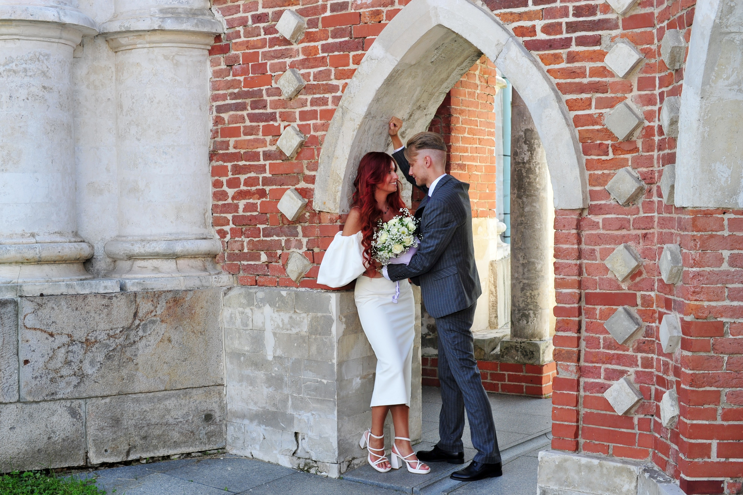 Свадьба в Царицыно летом, жених и невеста обнимаются и разговаривают в арке из красного кирпича