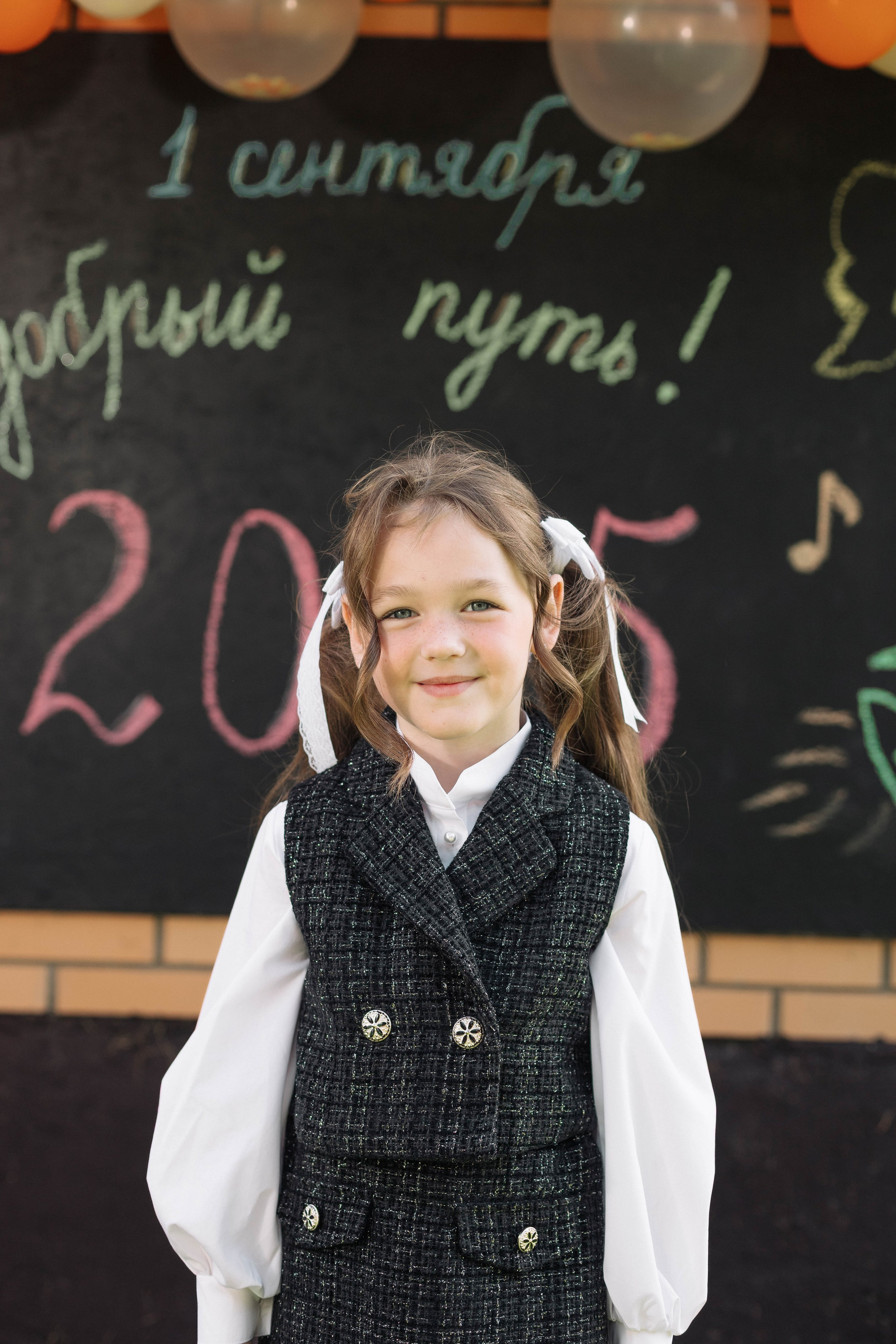 Крупный план первоклассницы на день сентября на фоне доски с поздравлениями