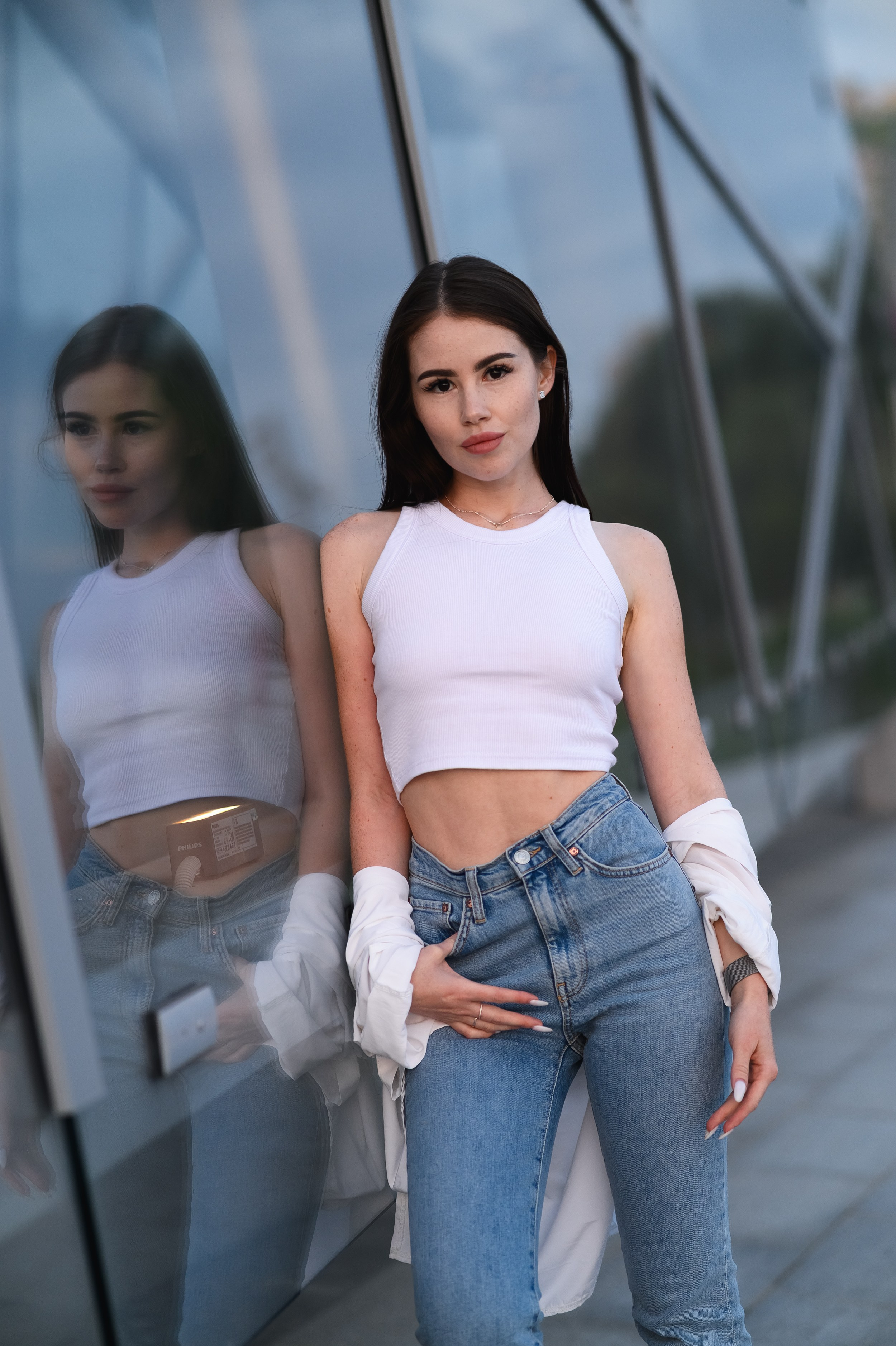 Фото девушки в белой рубашке и джинсах на фоне стеклянной стены театра Камала в Казани