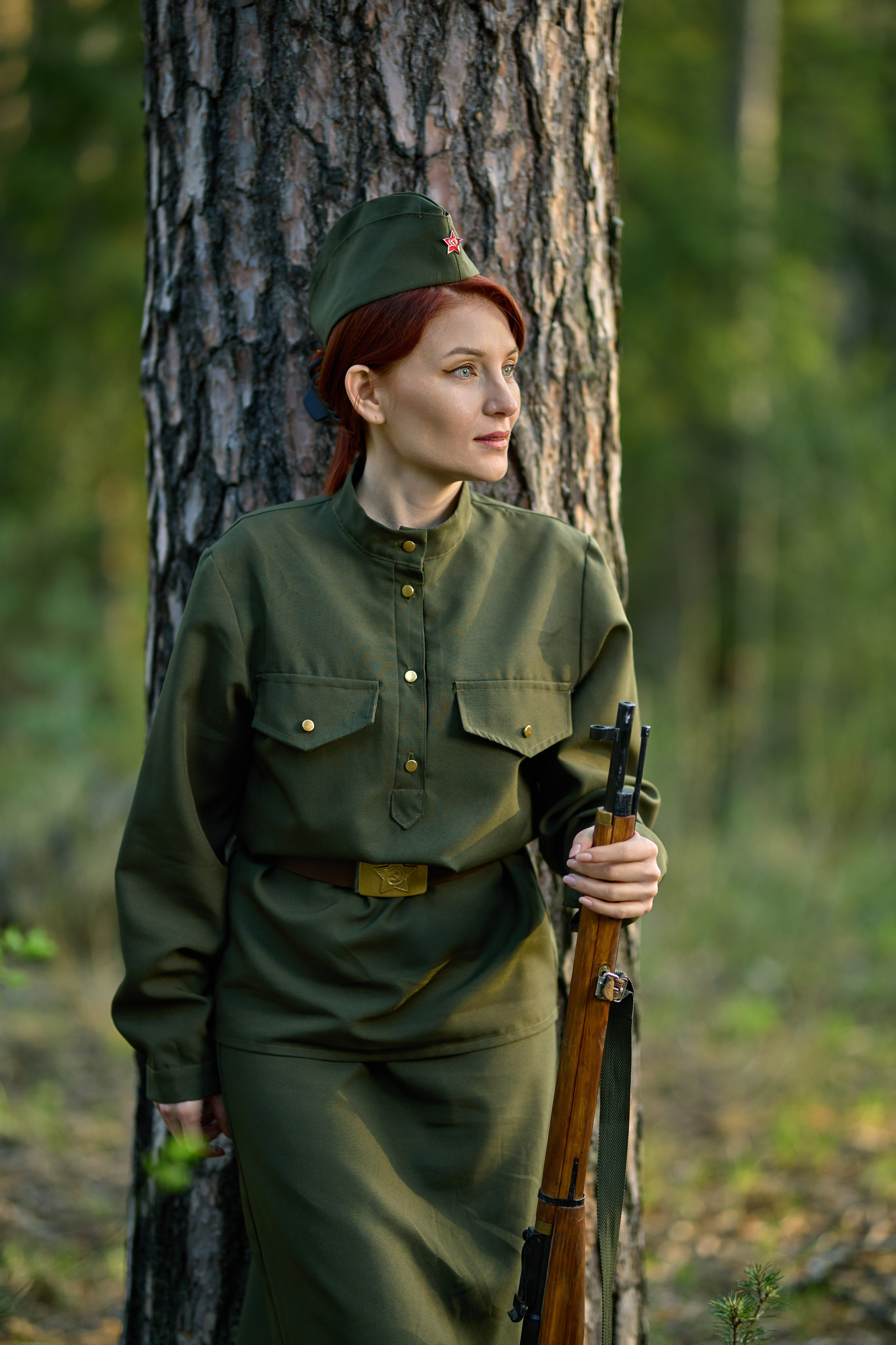 тематическая фотосессия на военную тему, девушка стоит с винтовкой в лесу около дерева
