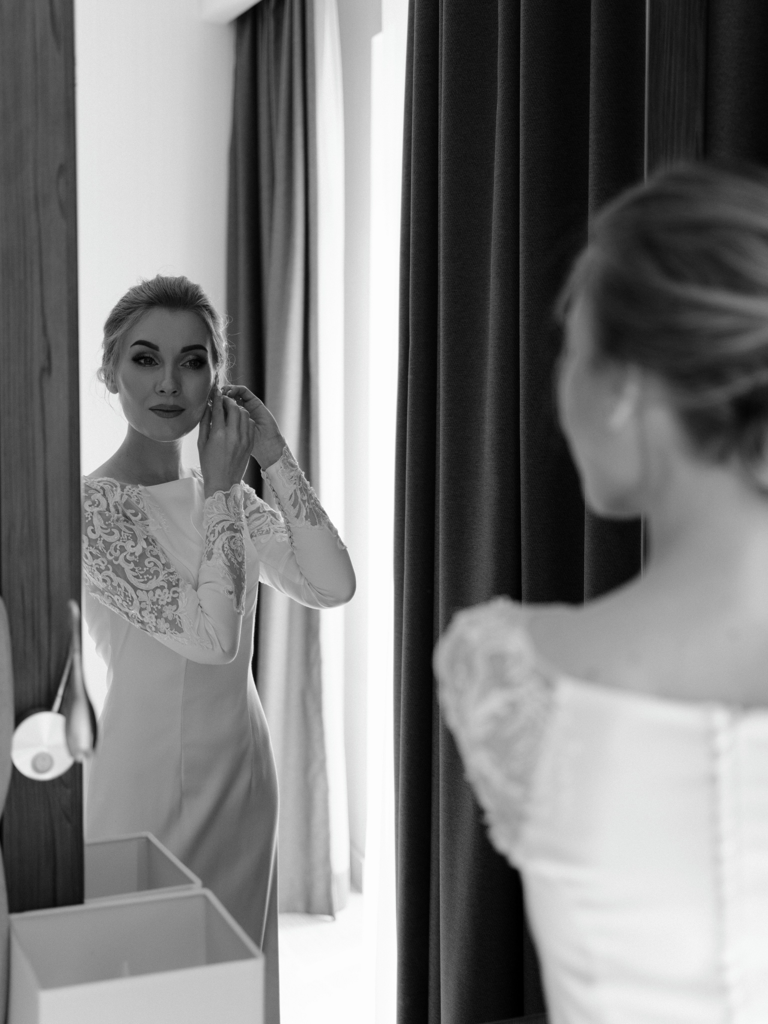 Невеста надевает серьги и смотрит в зеркало в отеле