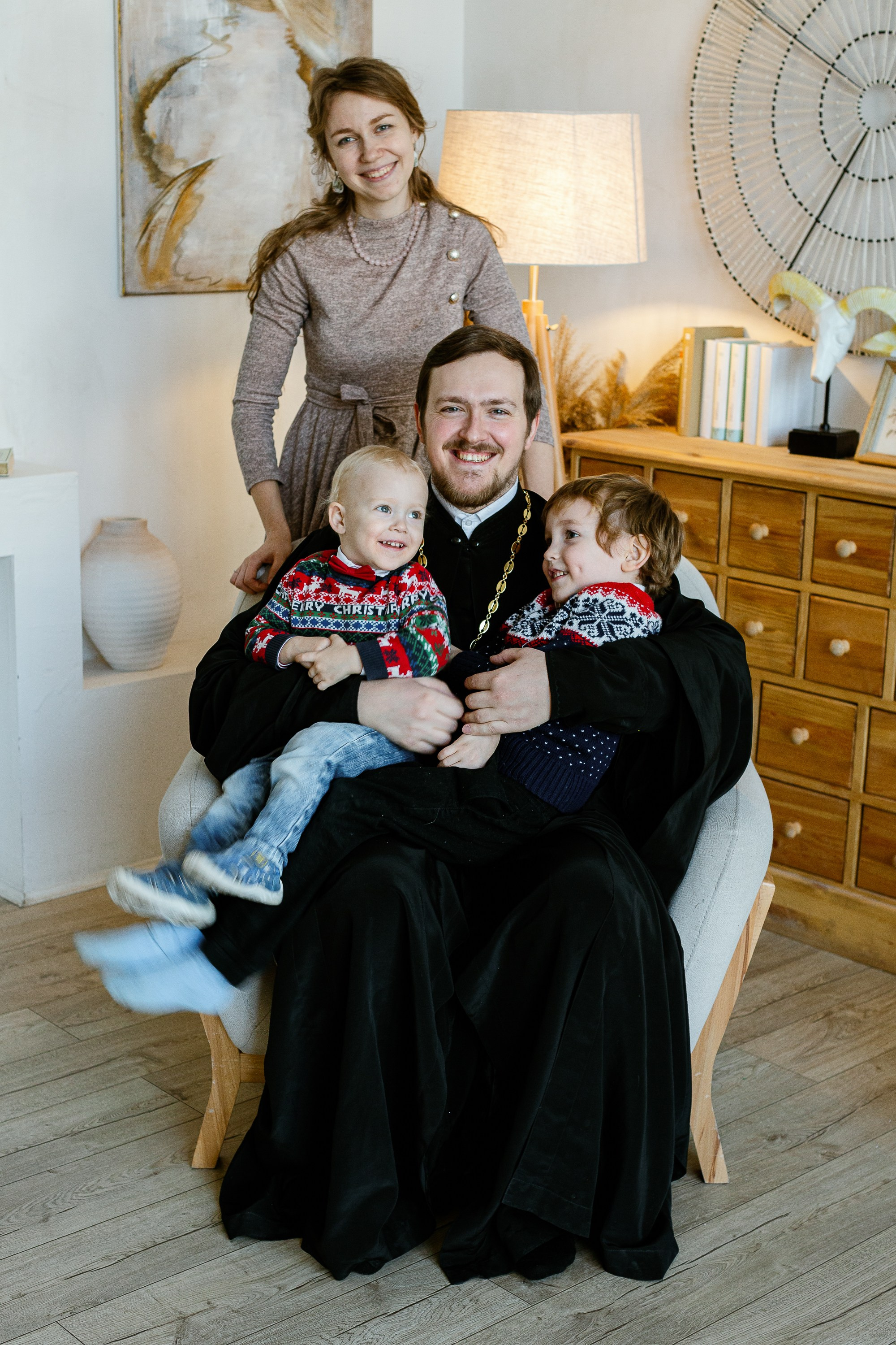 Семья священника. Отец сидит на кресле с детьми, жена стоит возле него.