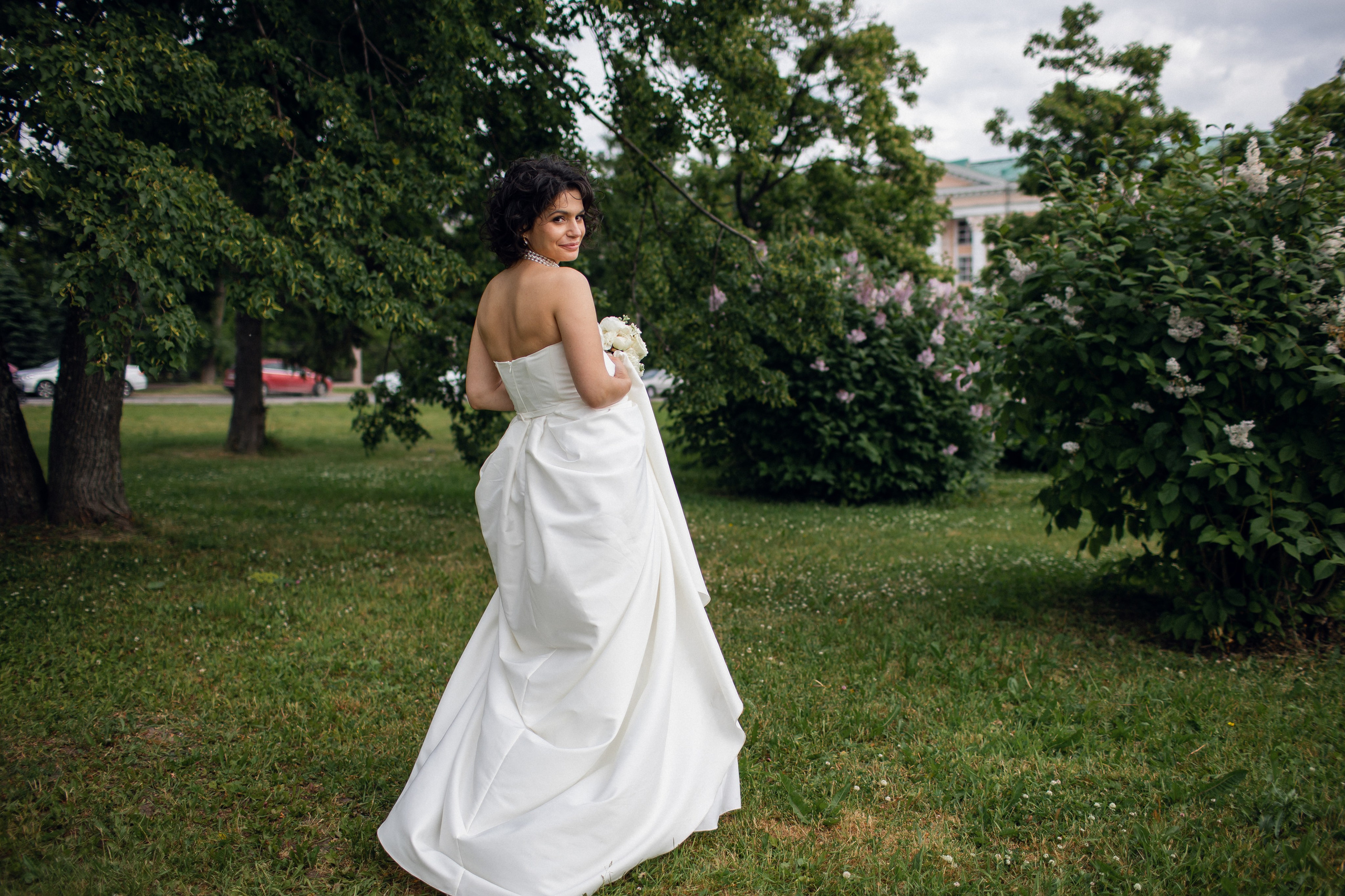 Игривые кадры для портфолио: невеста в свадебном платье дурачится среди зелени Центрального парка Архангельска с акцентом на динамику и натуральный свет