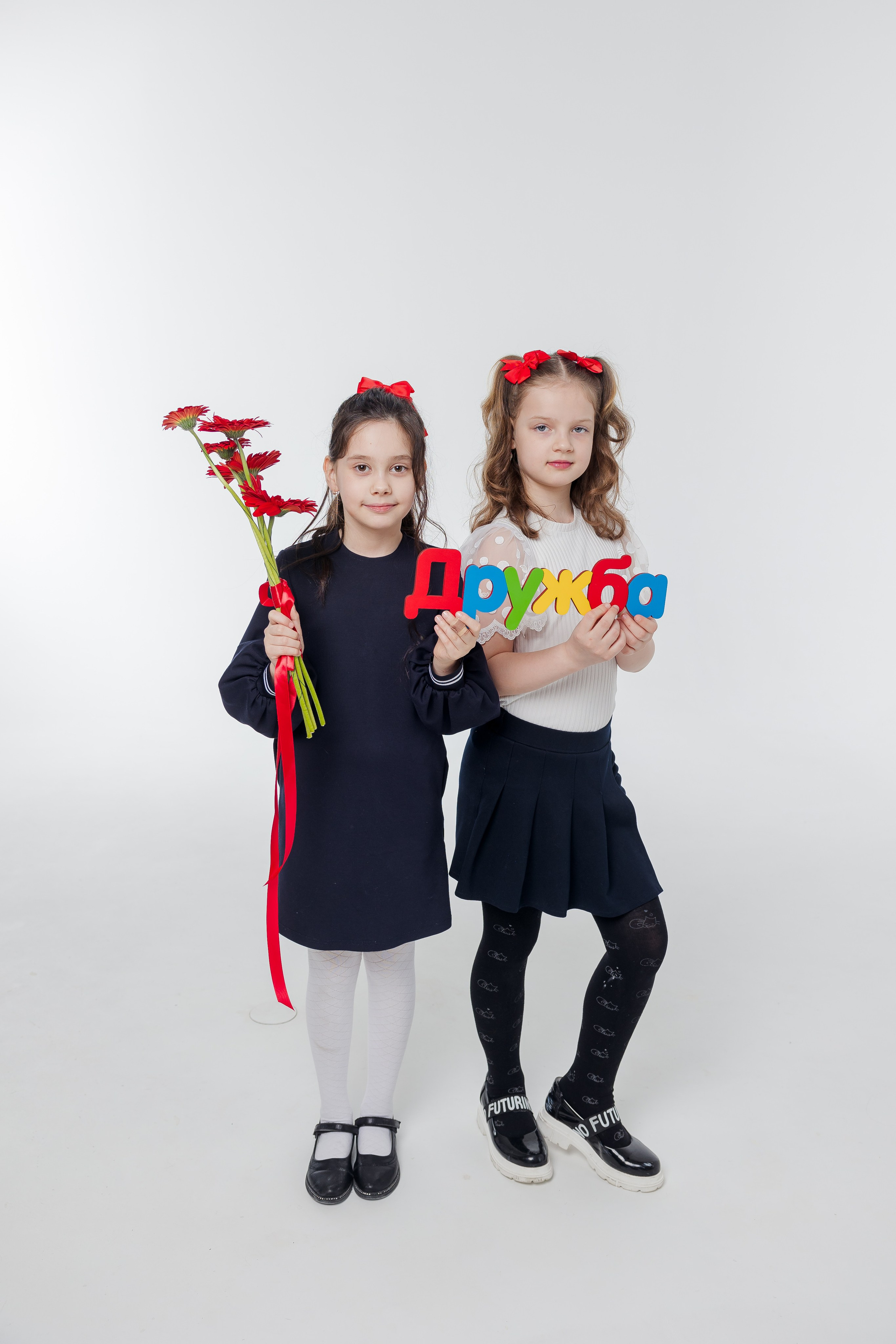 Две девочки стоят вместе в студии и держат надпись дружба