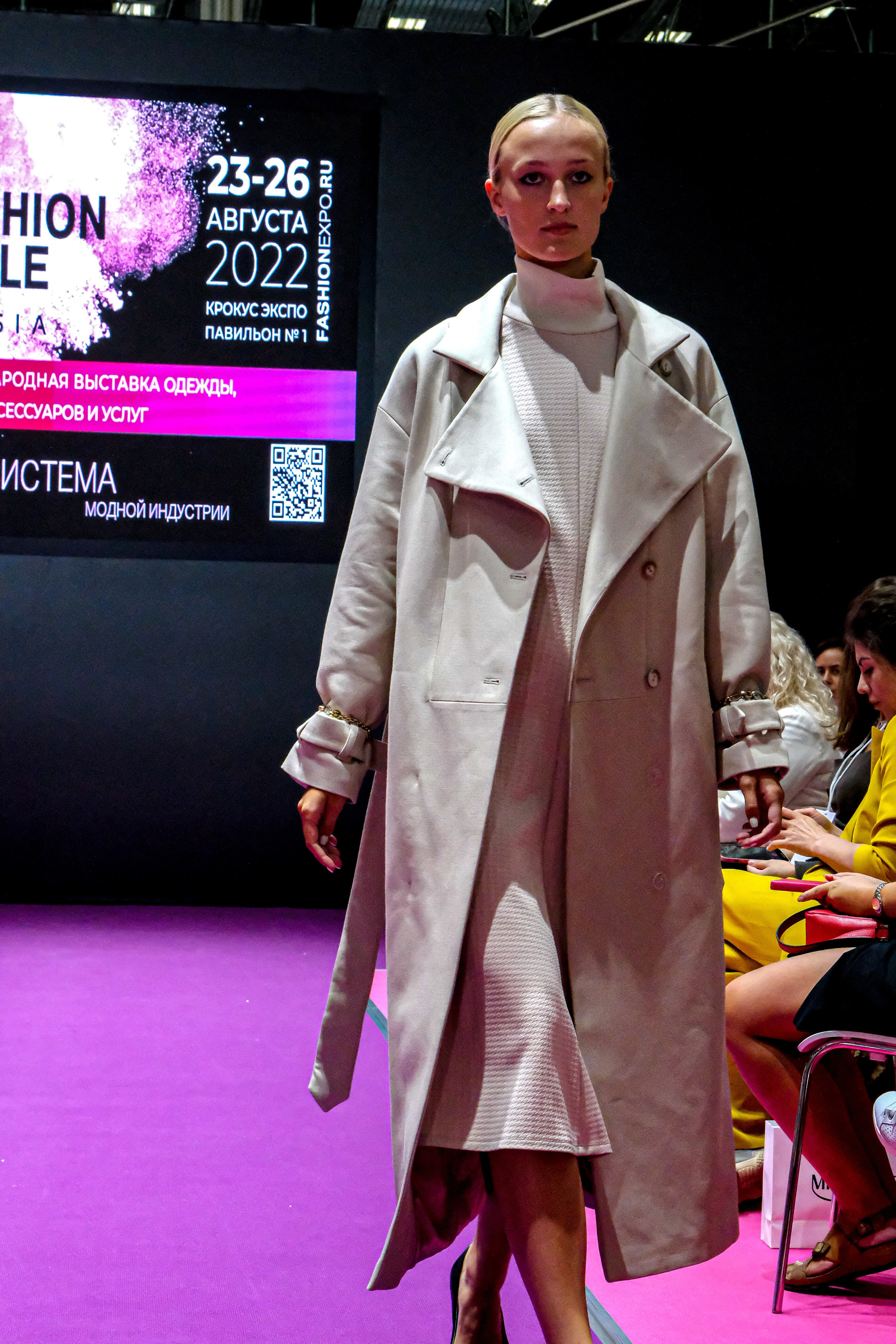  "Модели в ярких нарядах проходят по подиуму во время показа мод, освещенные яркими софитами и окруженные восторженными зрителями."