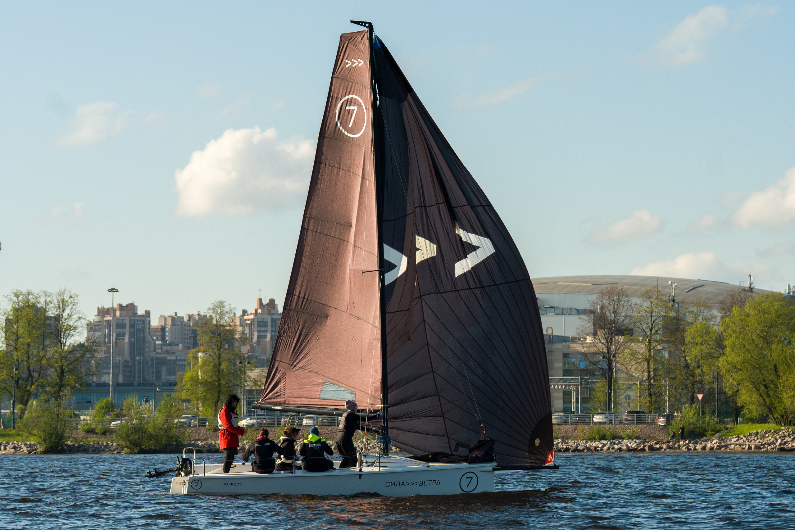 SV20 crew trims black sails on the Neva, Saint Petersburg behind