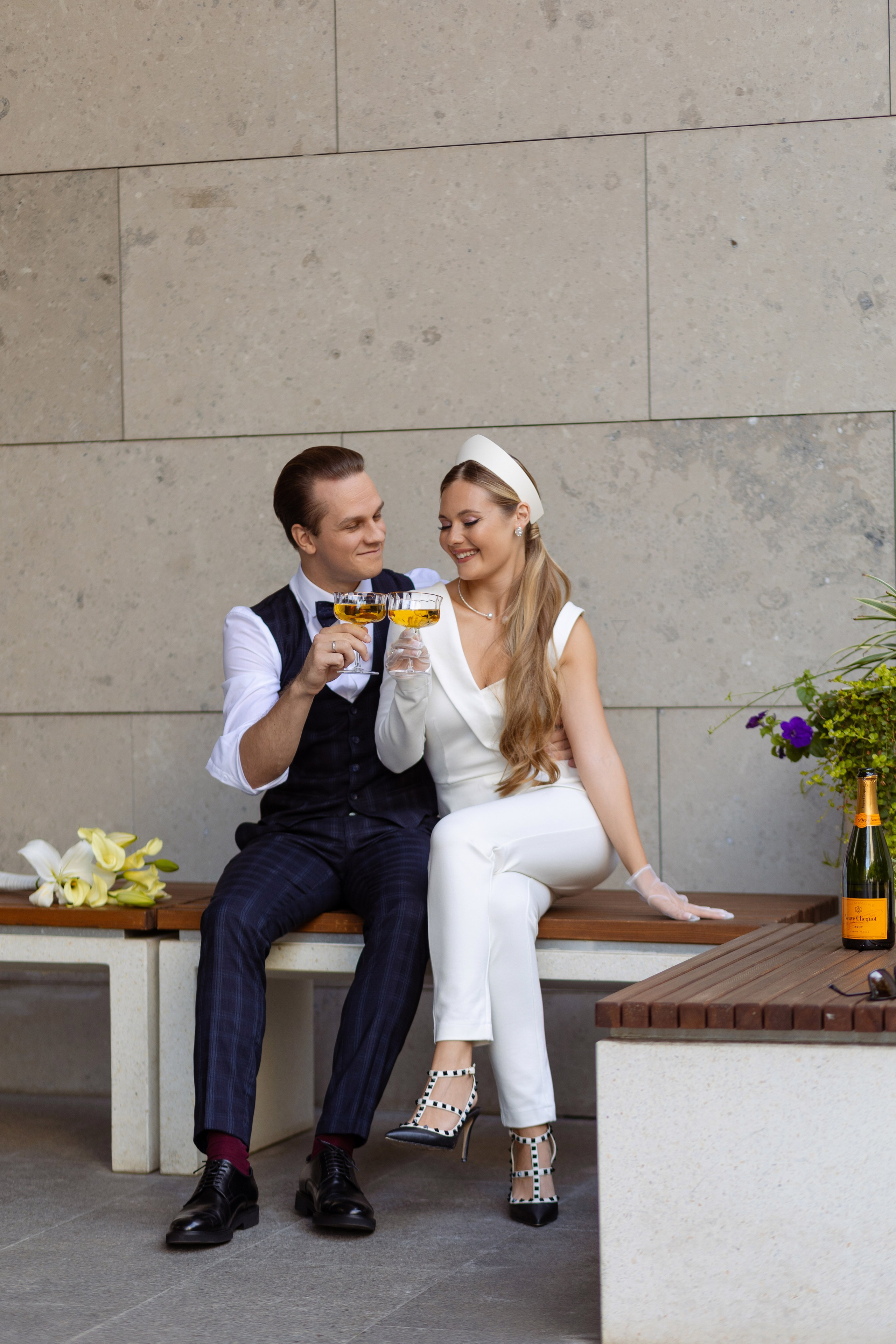 Жених с невестой сидят на лавочке с бокалами в руках.
