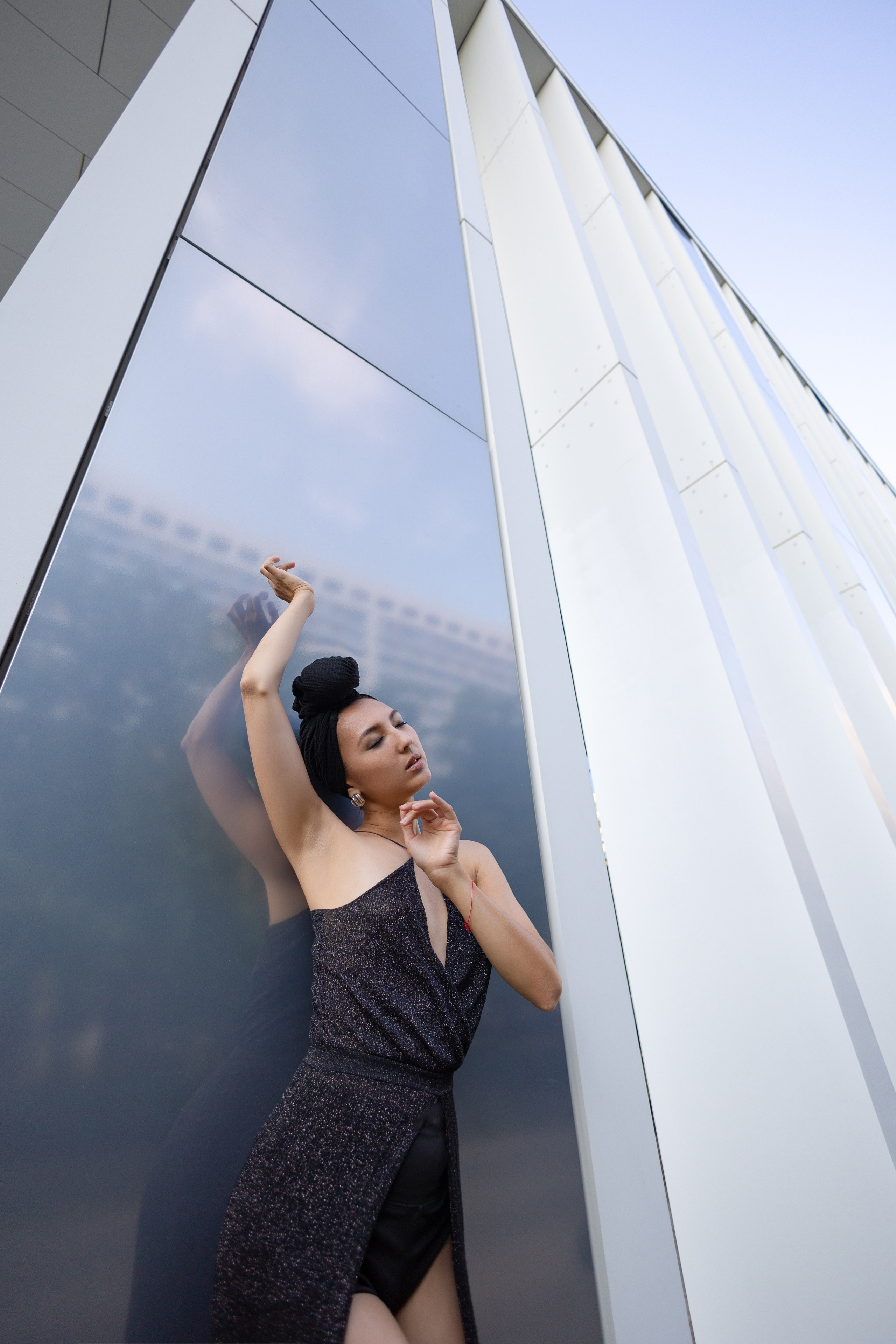 Девушка в чёрном блестящим платье позирует на фоне высокого небоскрёба