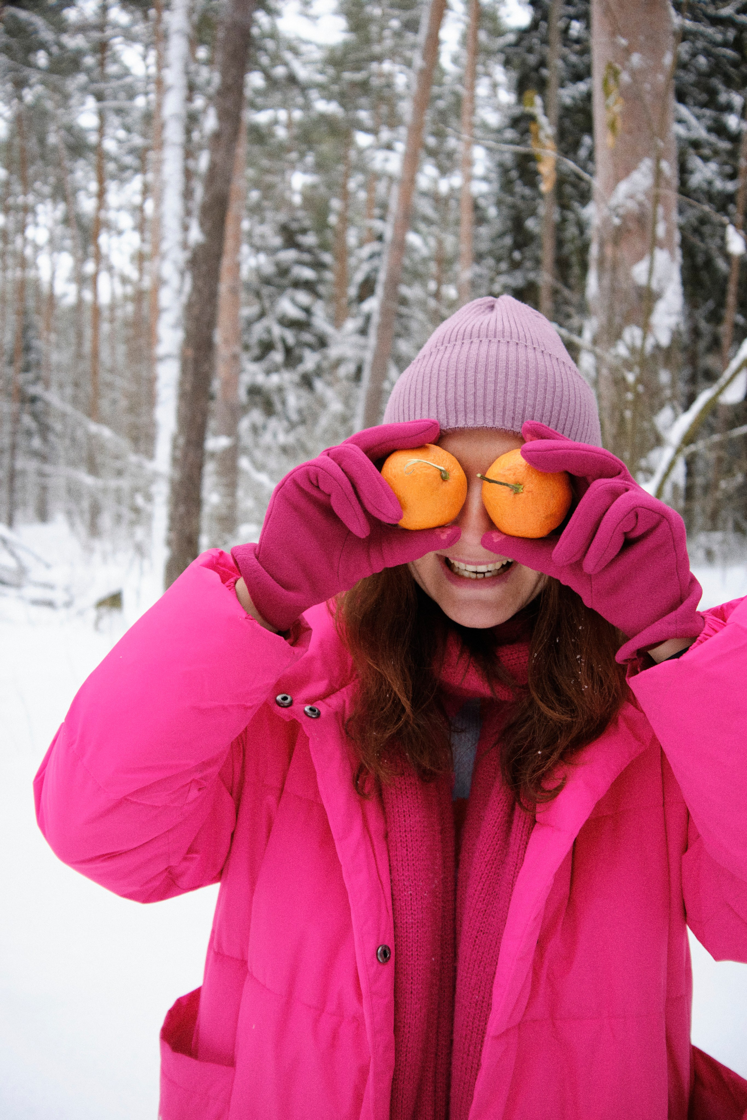 Девушка в яркой одежде в зимнем лесы закрыла глаза мандаринами