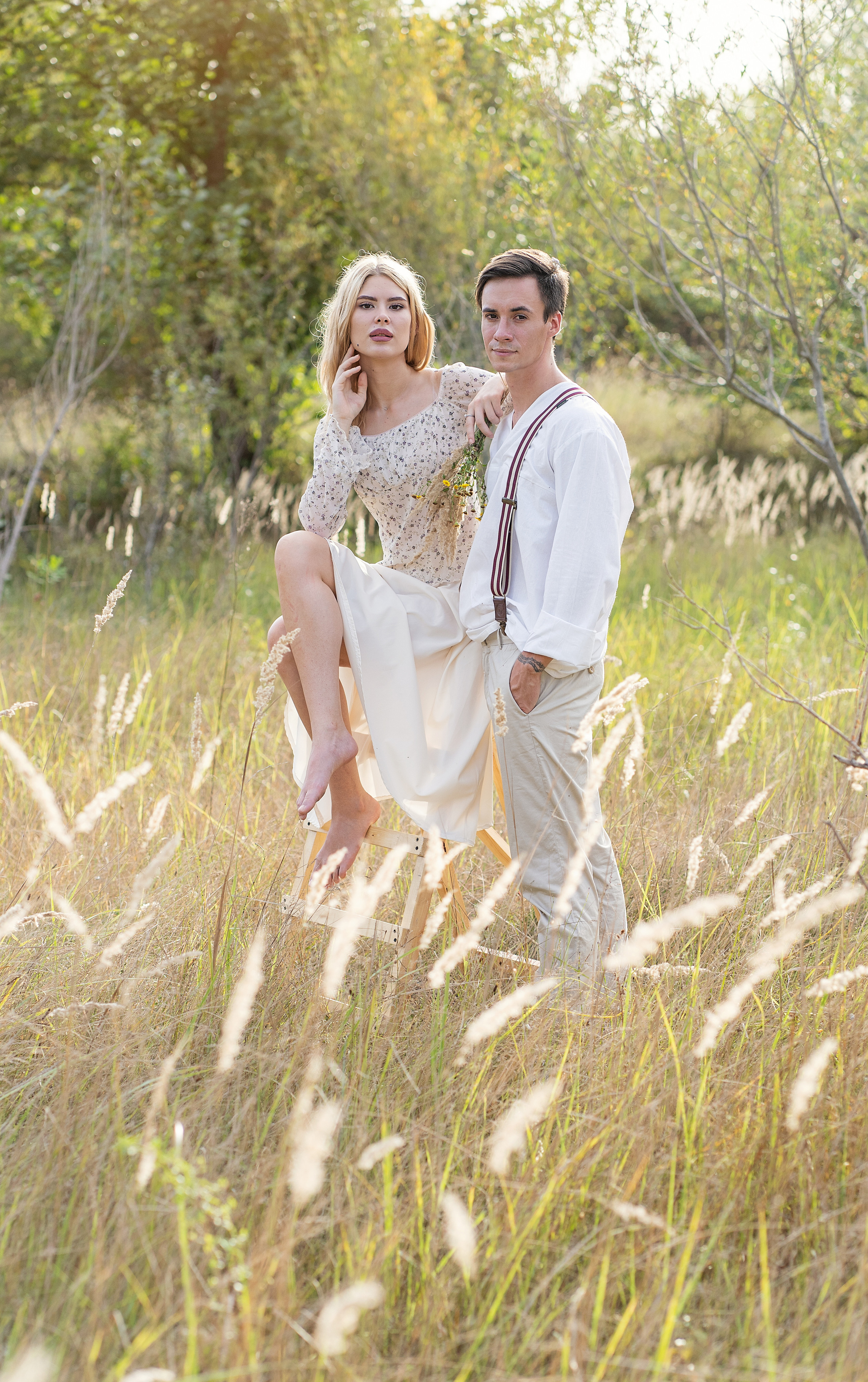 Пара в поле. Она сидит на возвышенности, он стоит рядом, оба смотрят в даль.