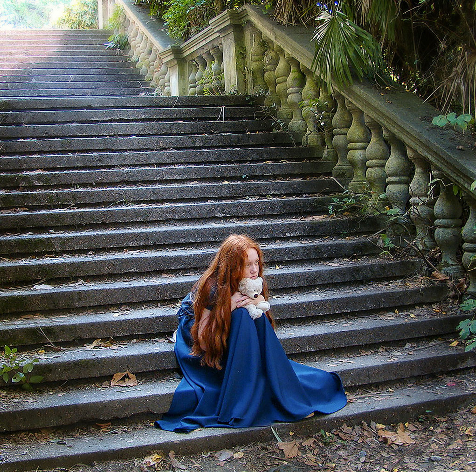 девочка в синем платье грустит на лестнице