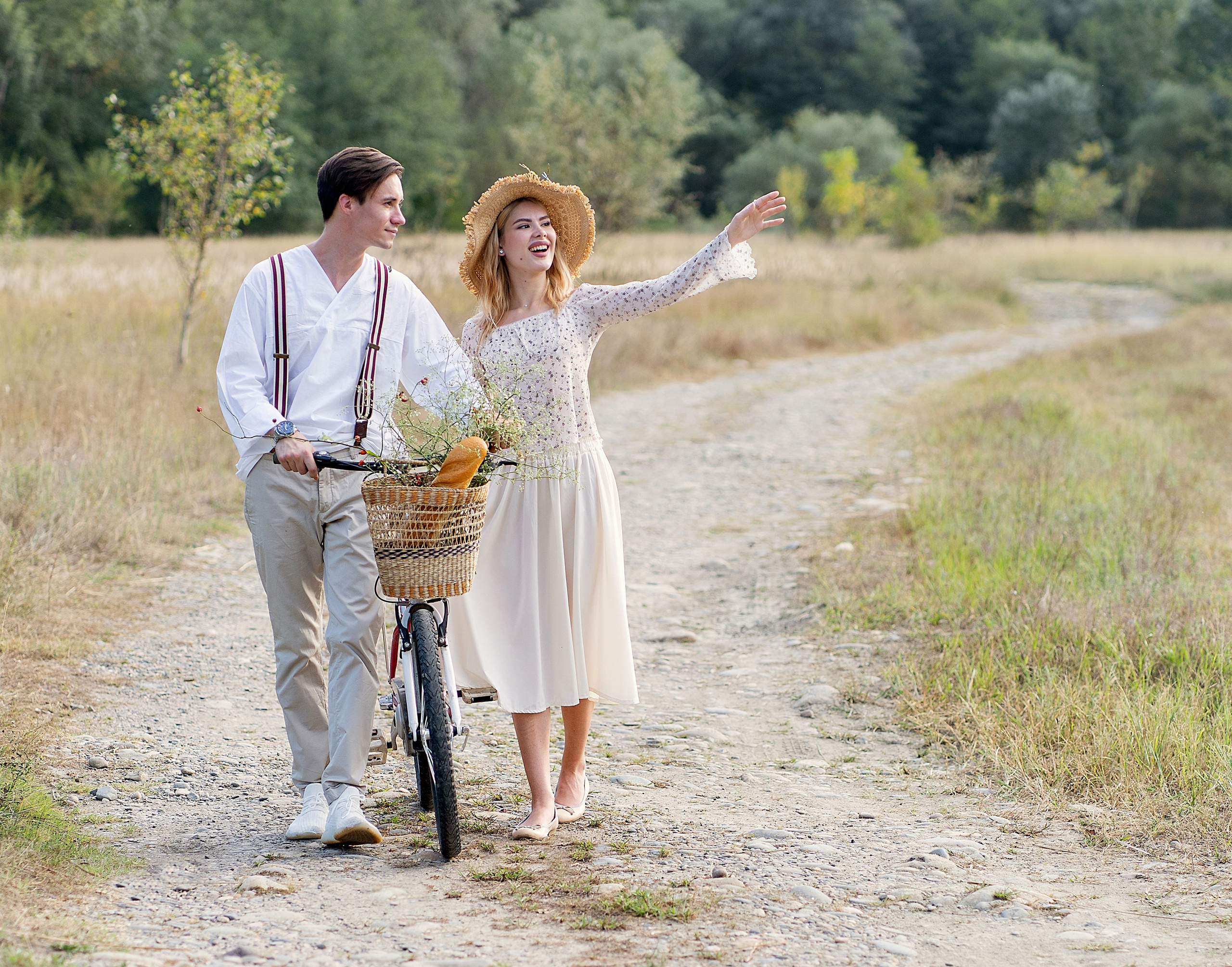 Двое идут на пикник по проселочной дороге, с велосипедом.