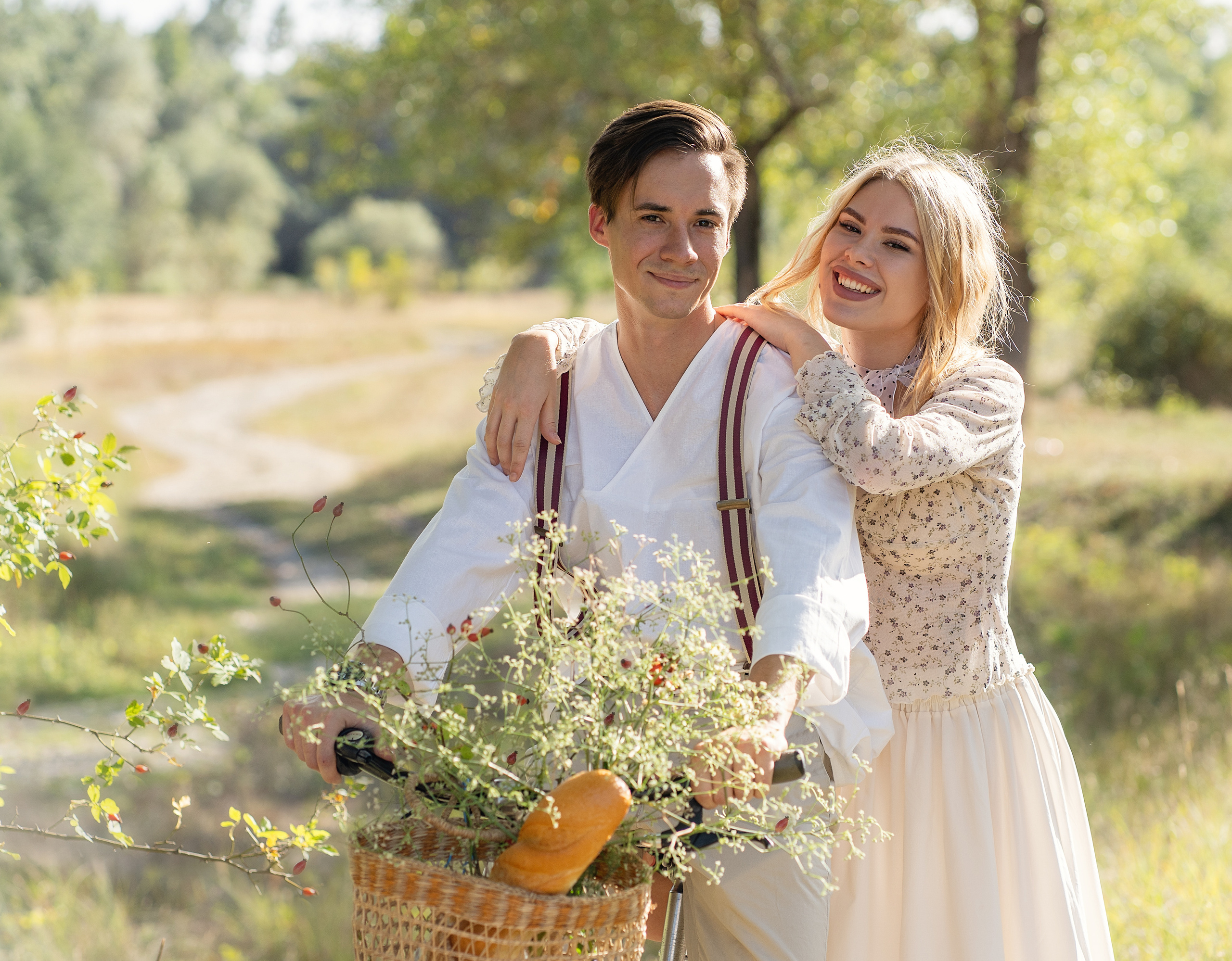 Парень сидит на велосипеде, девушка прильнула к нему сзади. Оба о чем-то смеются.