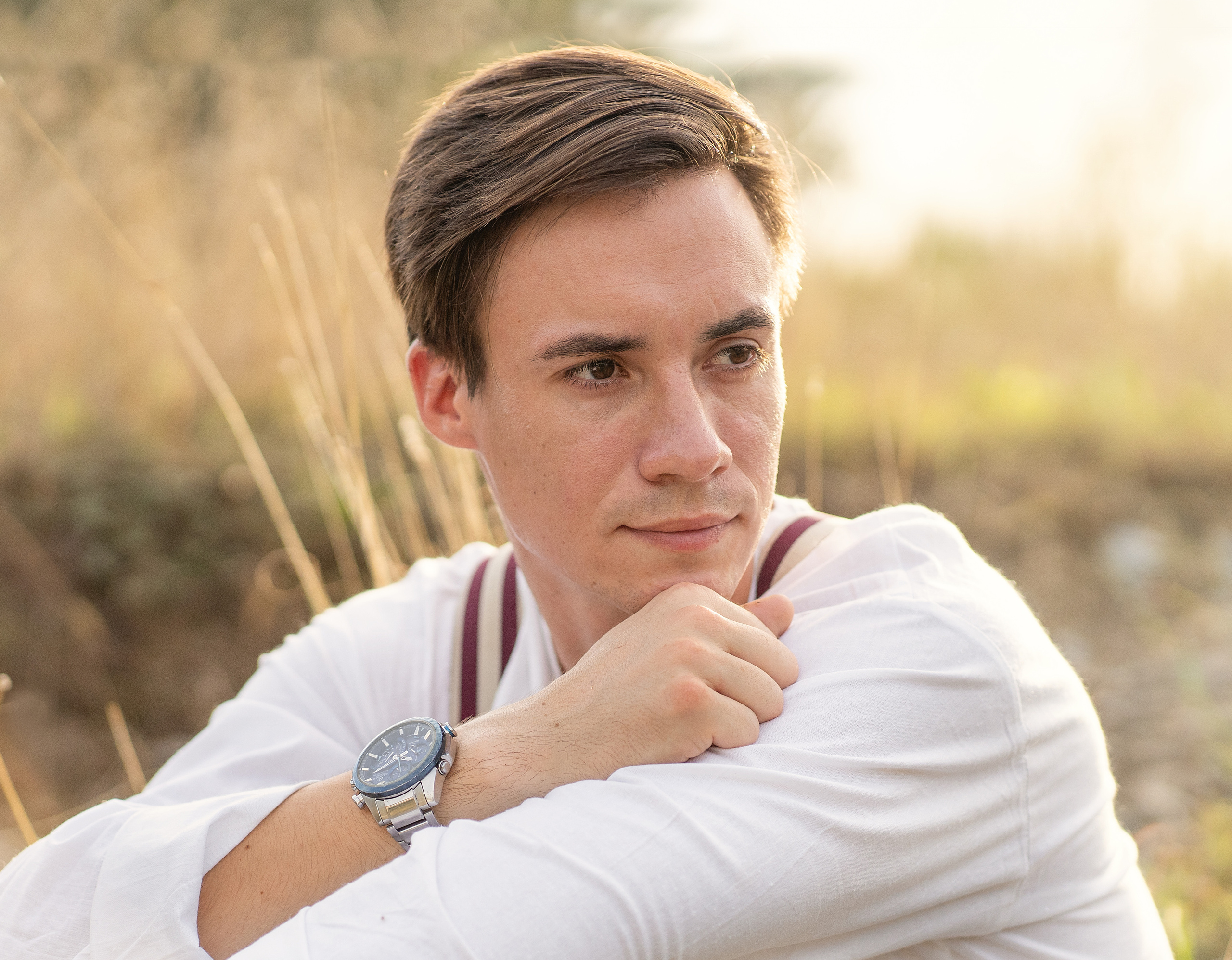 Мужской портрет. Парень сидит на пригорке, слегка задумавшись смотрит в сторону.