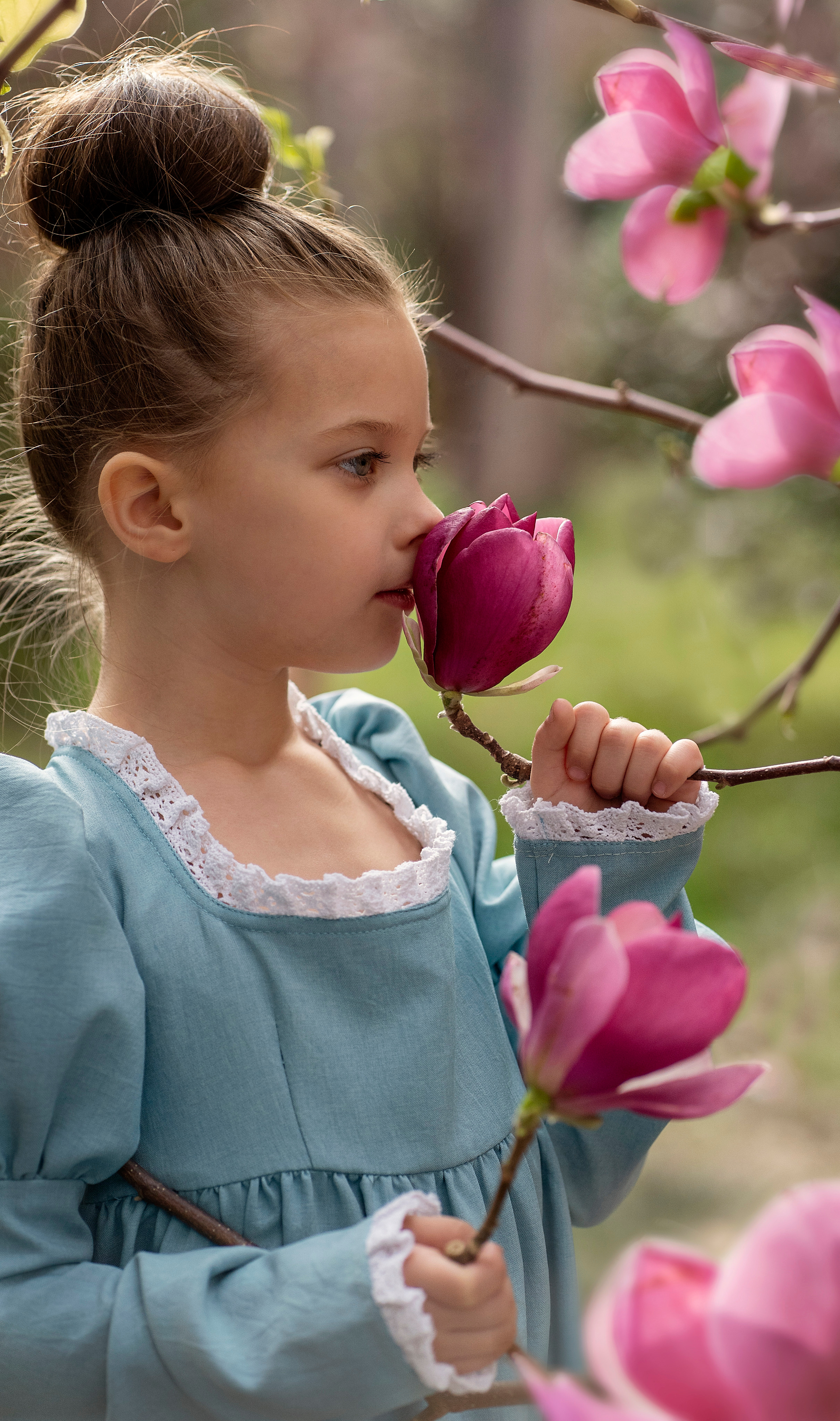 Девочка в винтажном платье нюхает бутон магнолии. Крупный план
