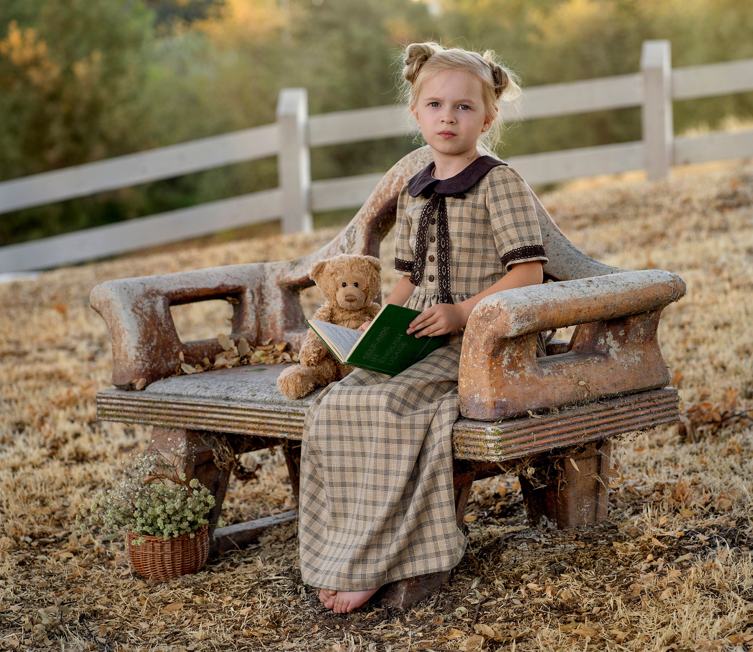 На лавочке сидит девочка, читает книжку своему плюшевому мишке.