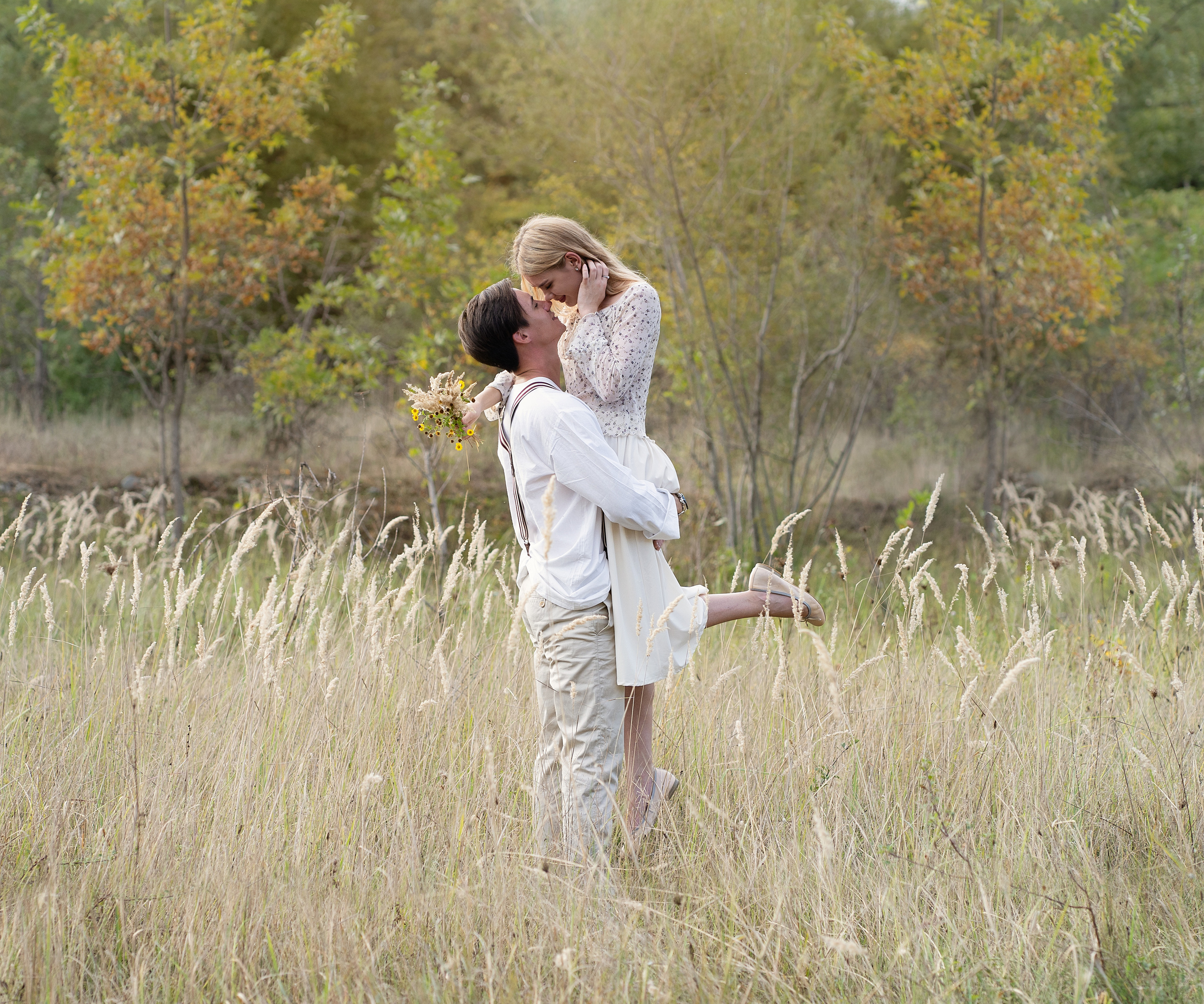 Парень кружит девушку в поле, на фоне осеннего леса.
