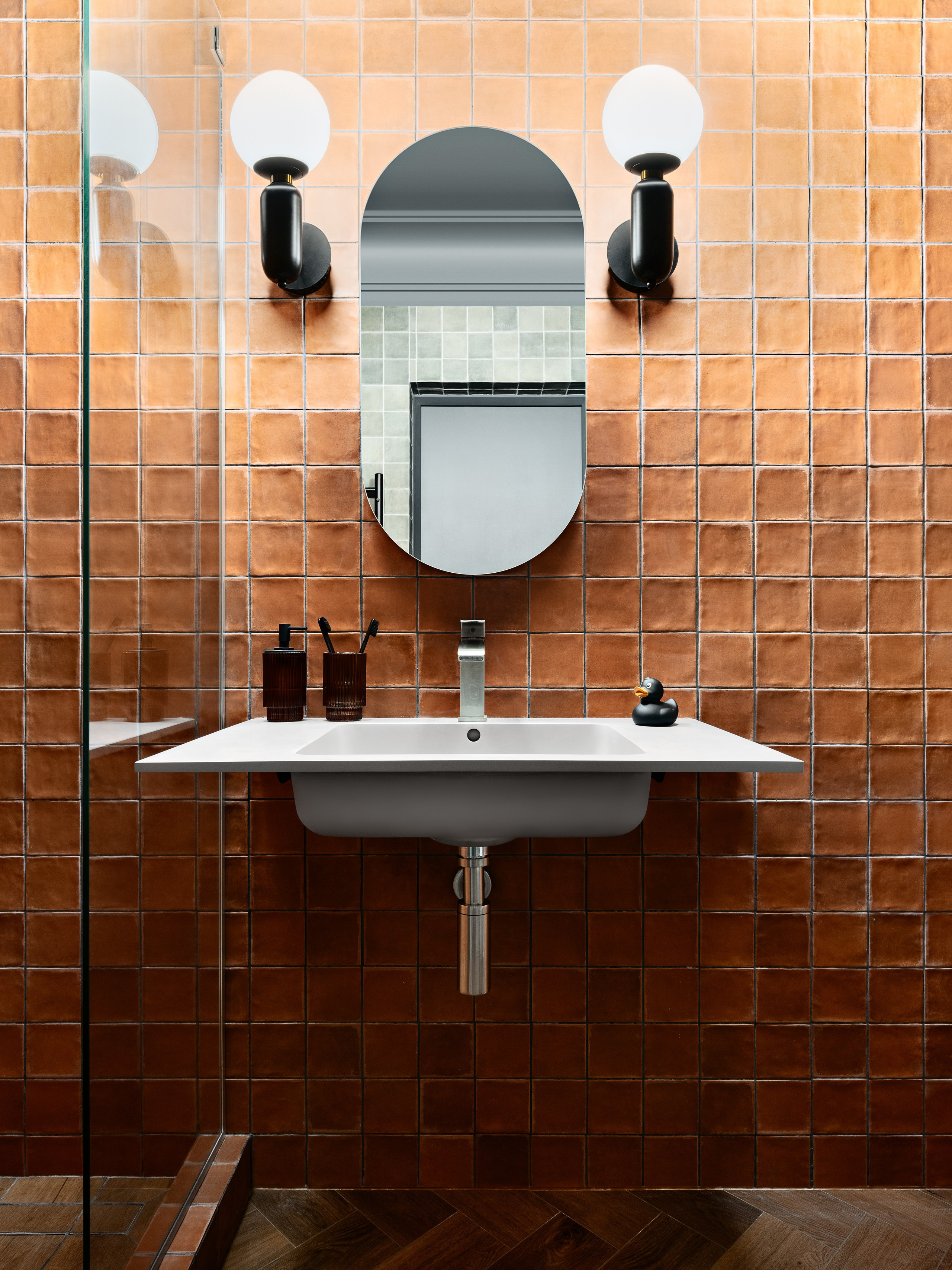 Уютная ванная в современном стиле с матовой терракотовой плиткой, подвесным зеркалом, черными светильниками и деревянным полом; авторский проект дизайнера Антона Логинова, стилистика Алёны Мощенской, фотография Сергея Денисенко.