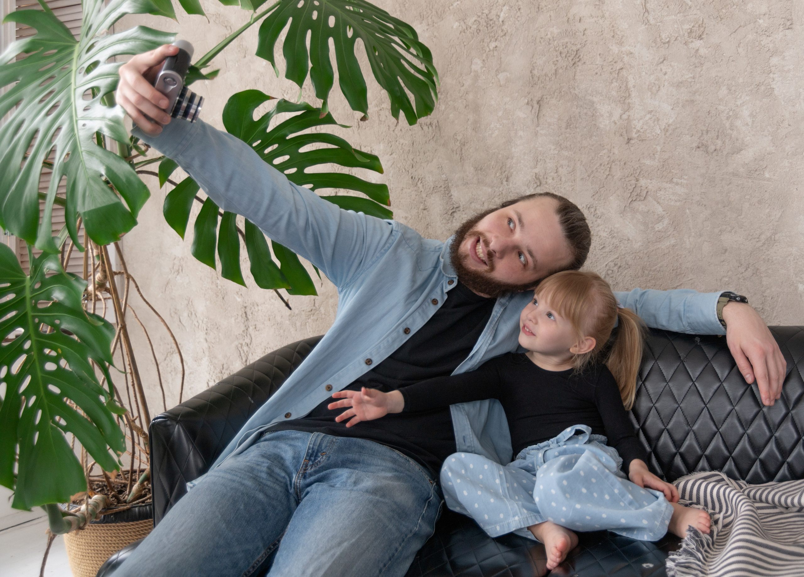 Папа с дочкой делают селфи на диване, смеются и дурачатся — живая и искренняя эмоция в семейной фотосессии.