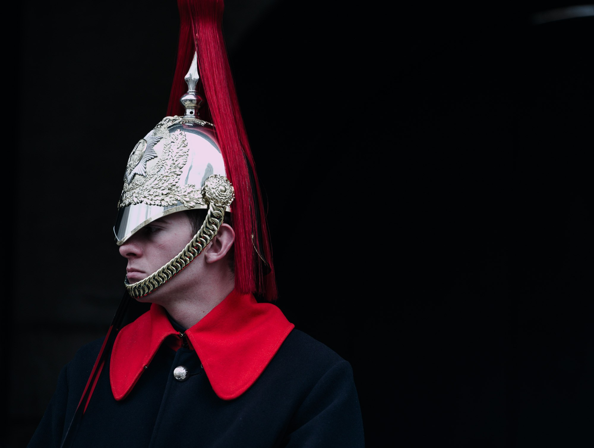 Крупный план портрета гвардейца Королевской конной гвардии, резкий фокус на деталях металлического шлема и ярко-красном воротнике, драматичное освещение