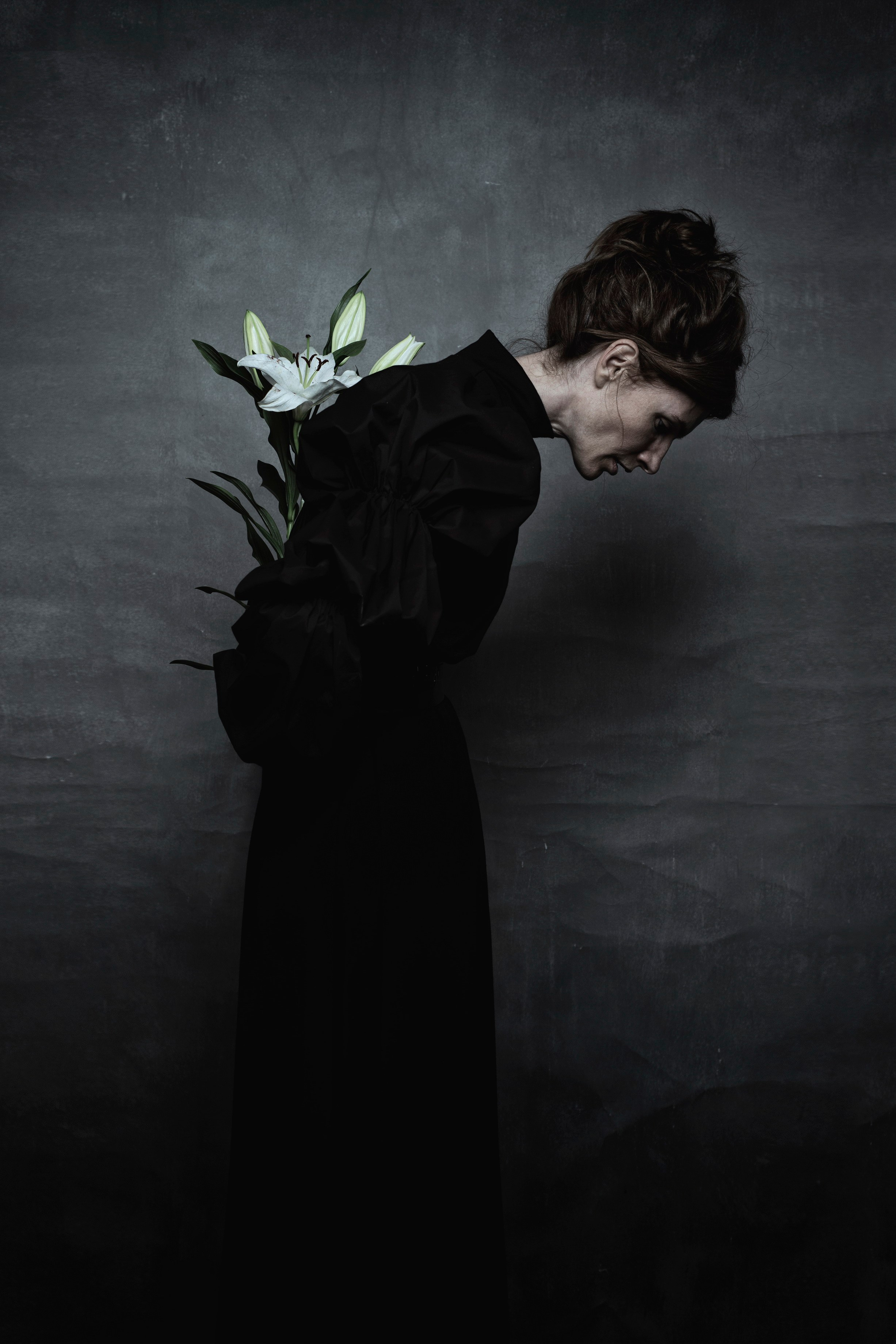 Девушка с лилией в черном платье на сером фоне 