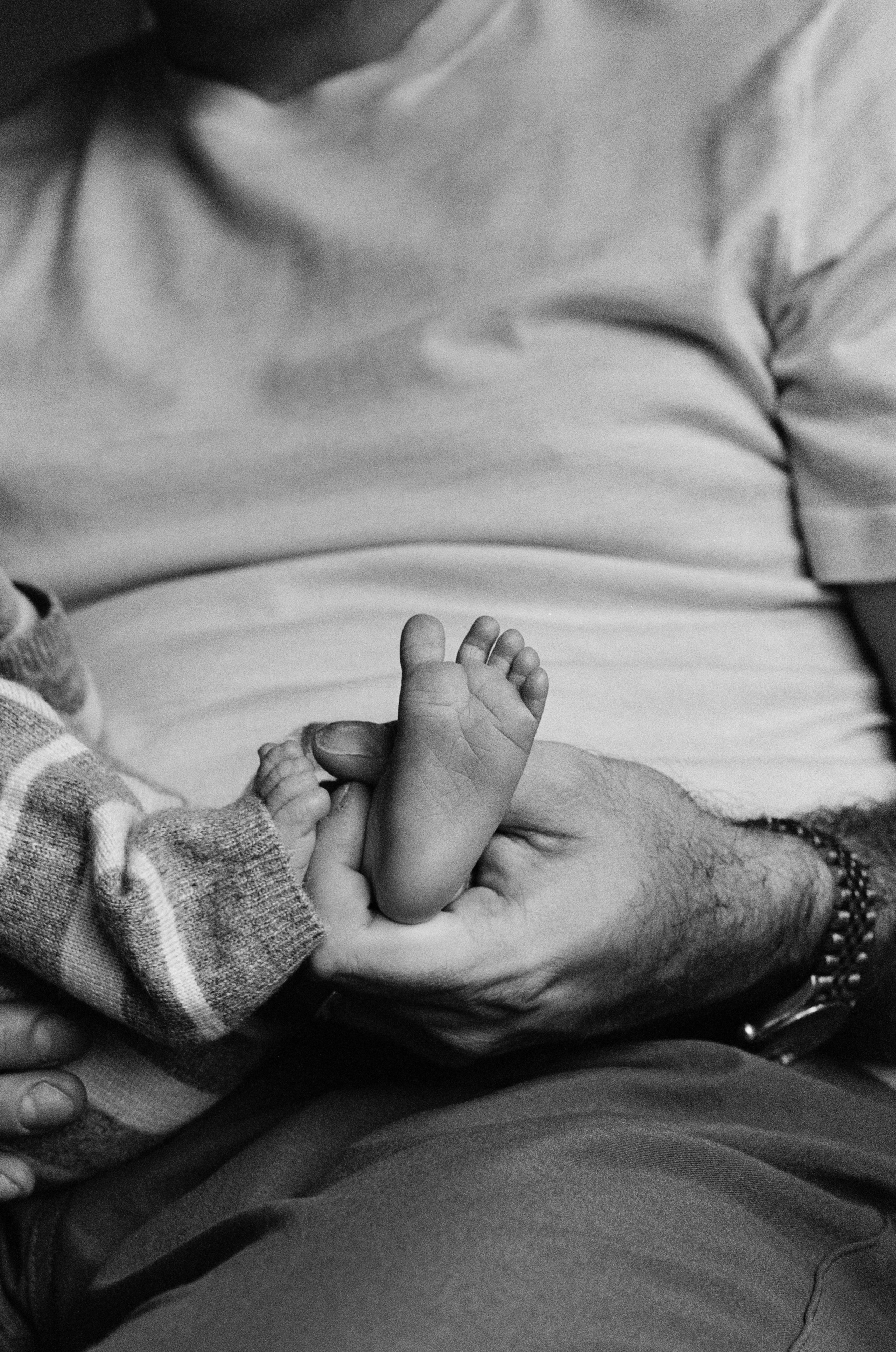 A dad holds his newborn son's foot, a lifestyle newborn film photo