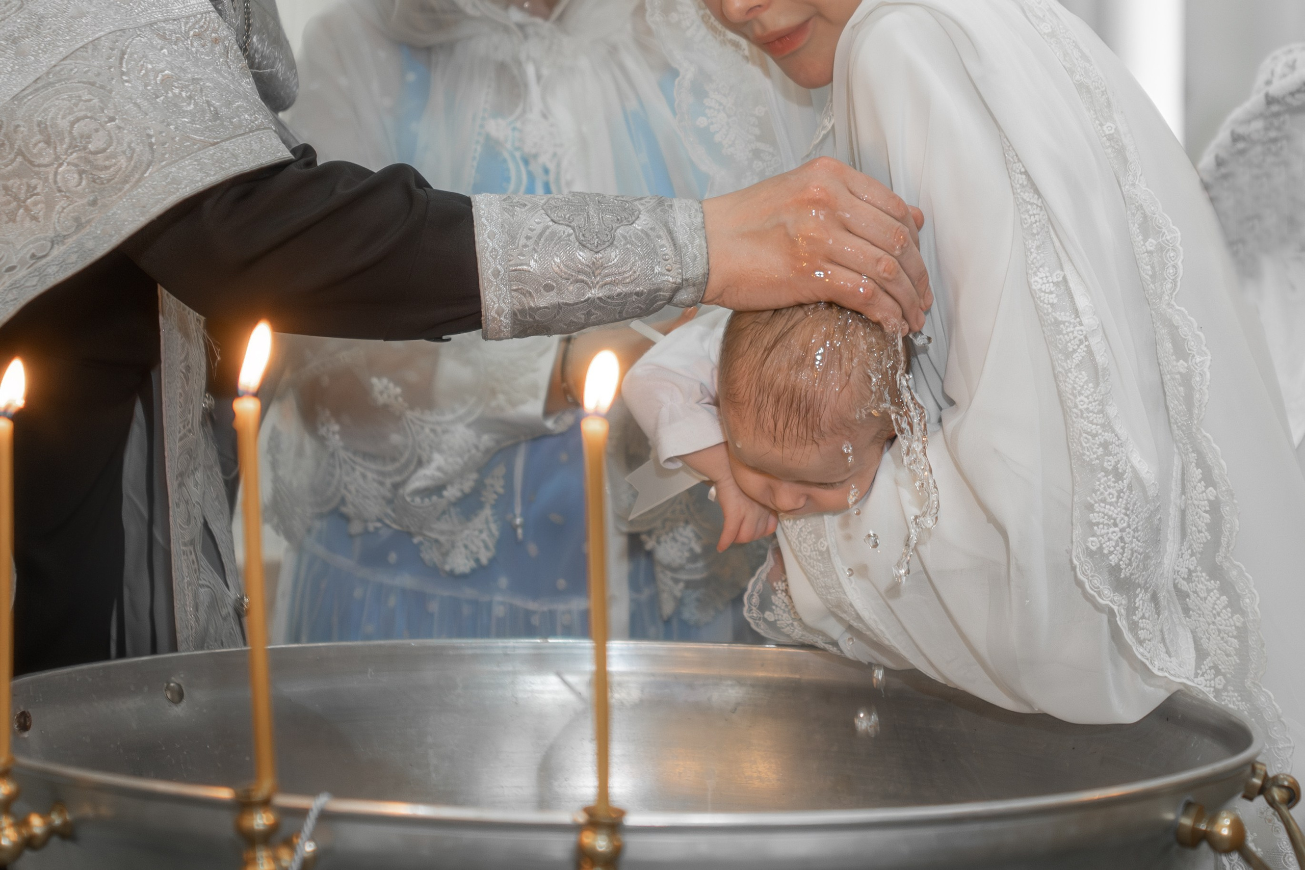 священник над купелью поливает водой на голову малышке 