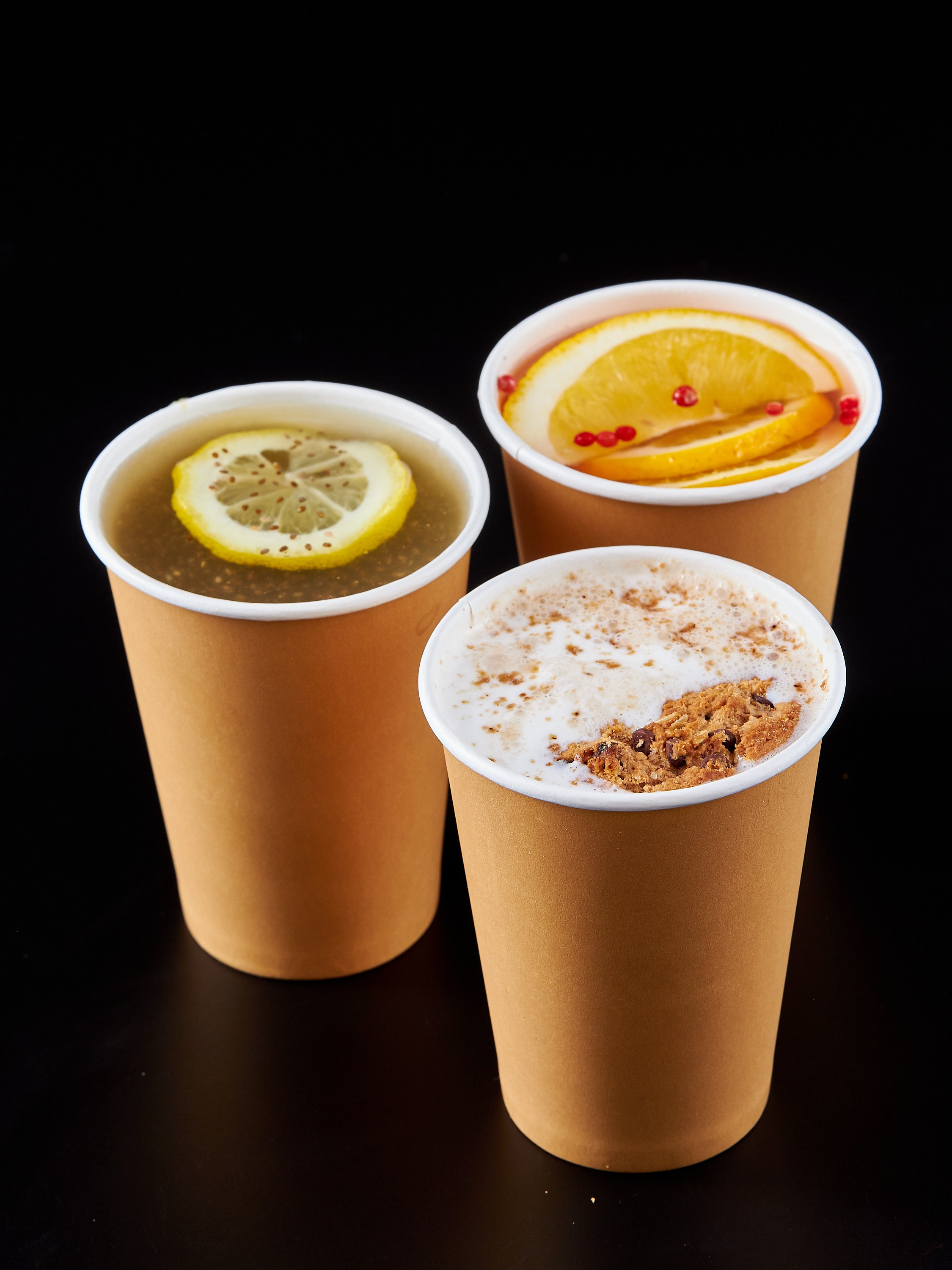 Коктейли в трех бумажных стаканах на черном фоне