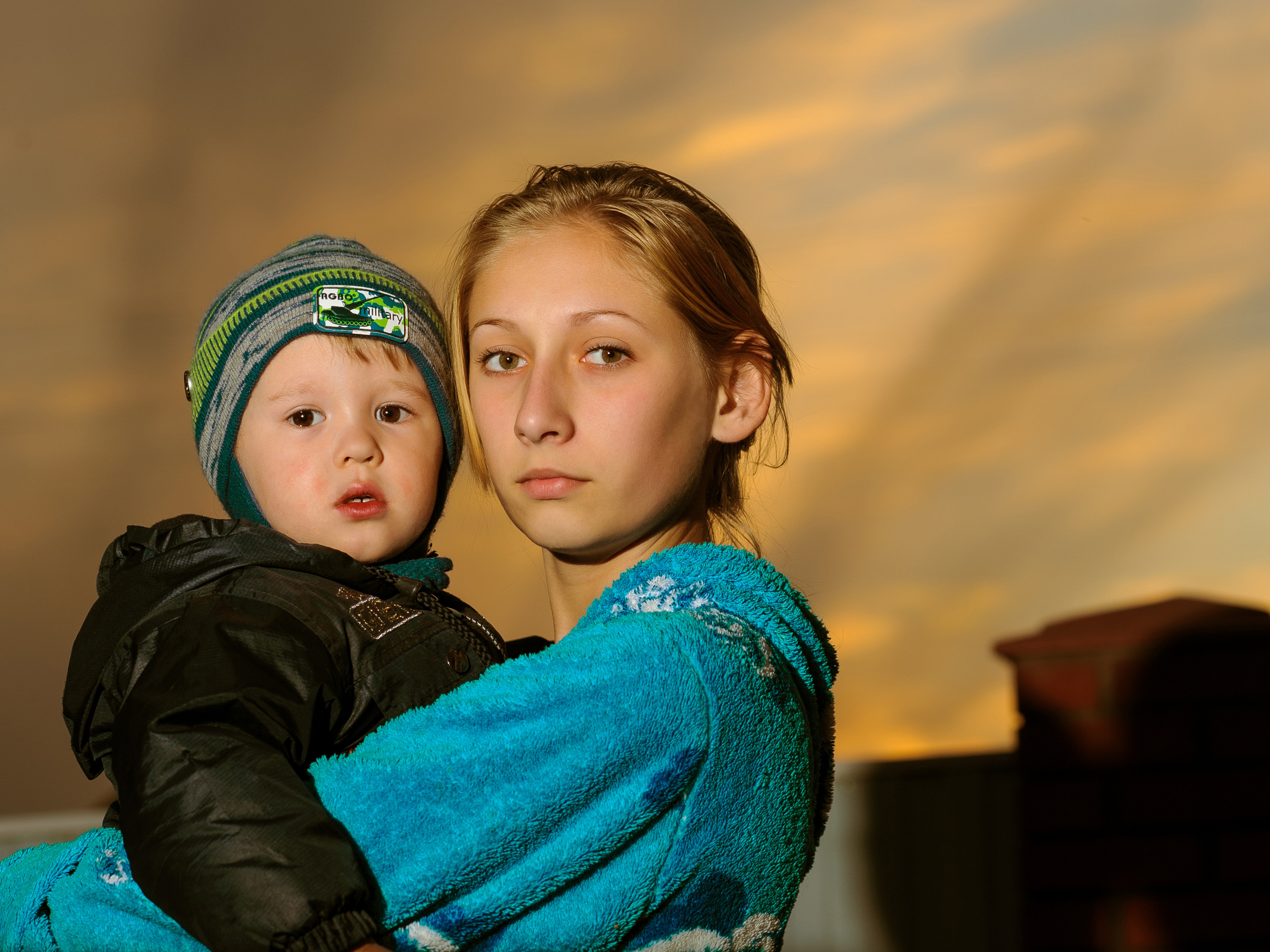 старшая сестра держит на руках младшего братика на фоне заката