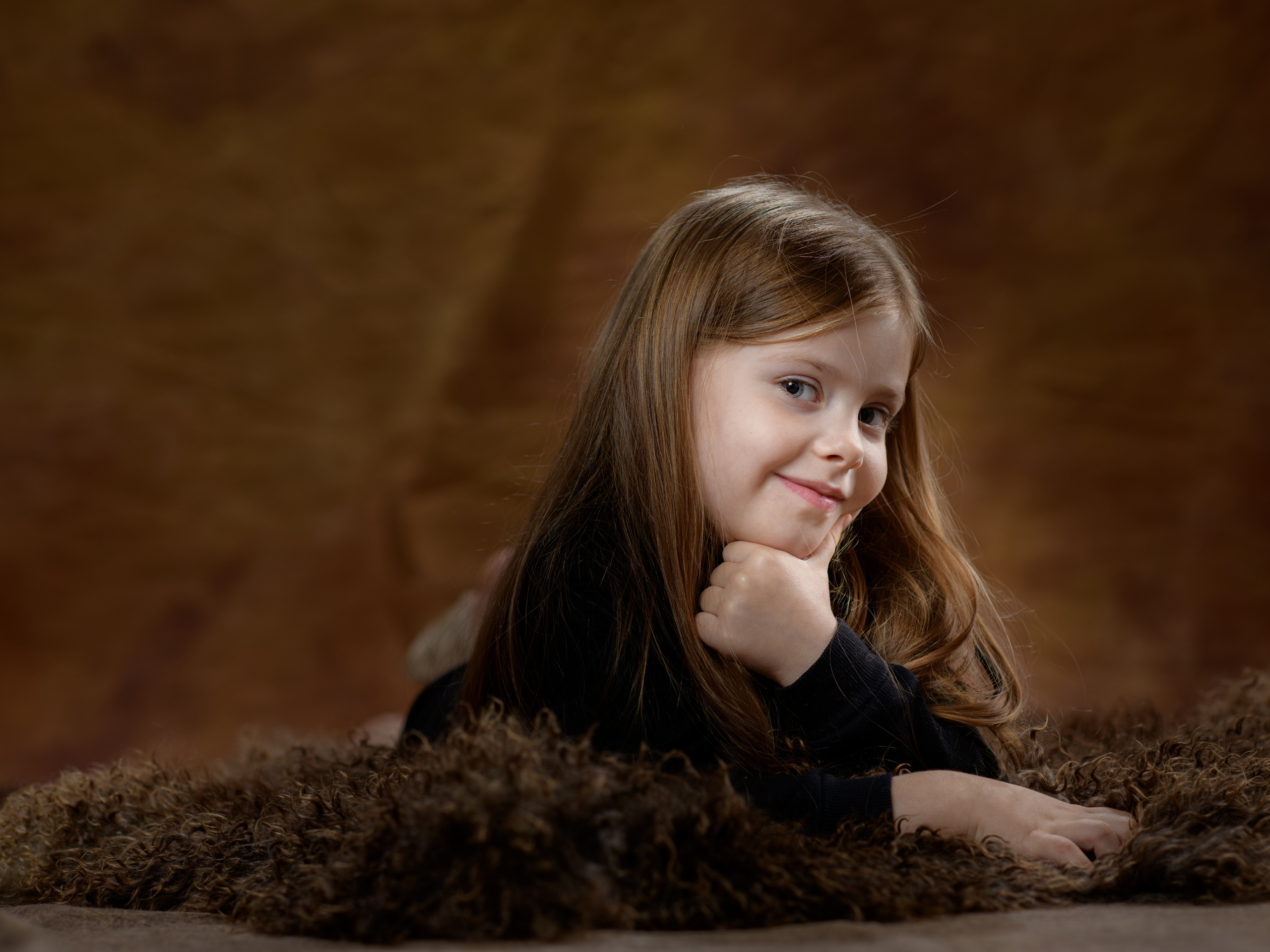 девочка на фотосессии игриво смотрит на камеру подставив ручку под подбородок