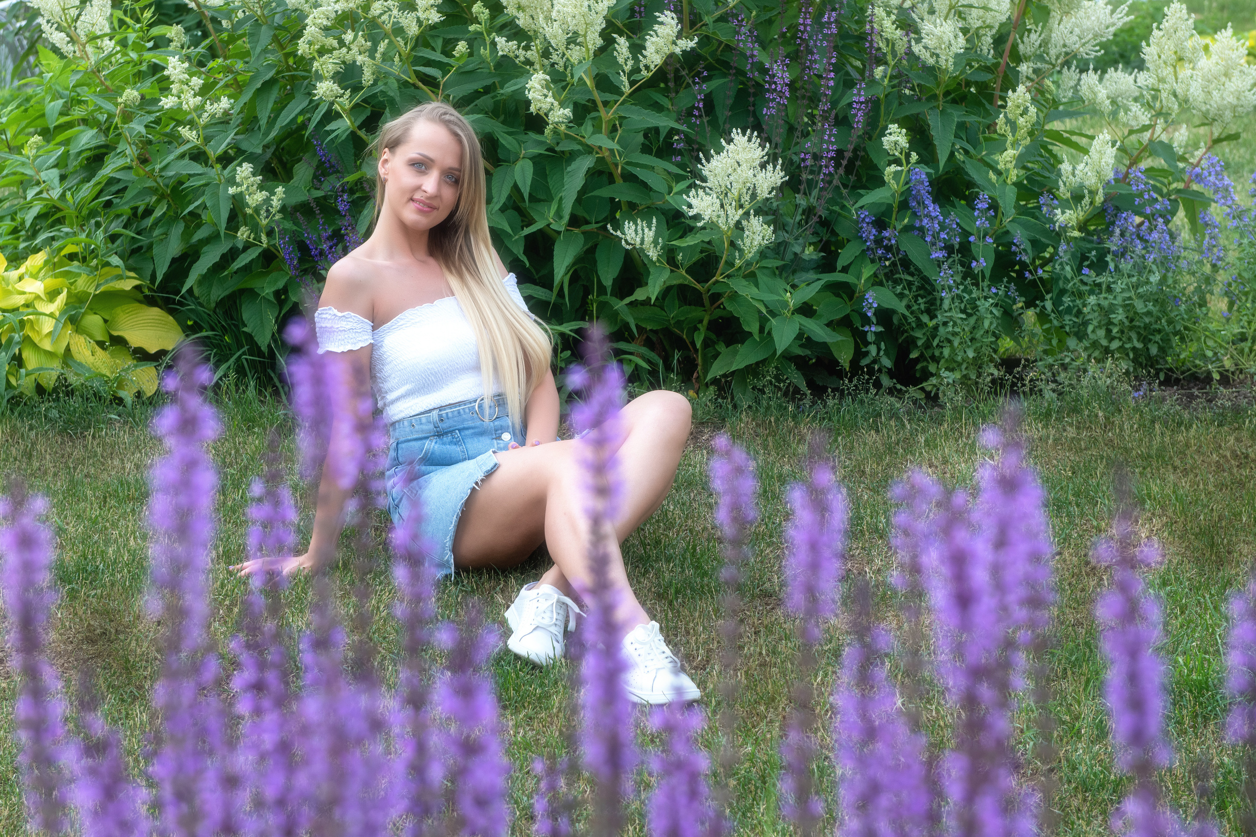 Сидящая на траве девушка смотрит на сиреневые цветы впереди себя