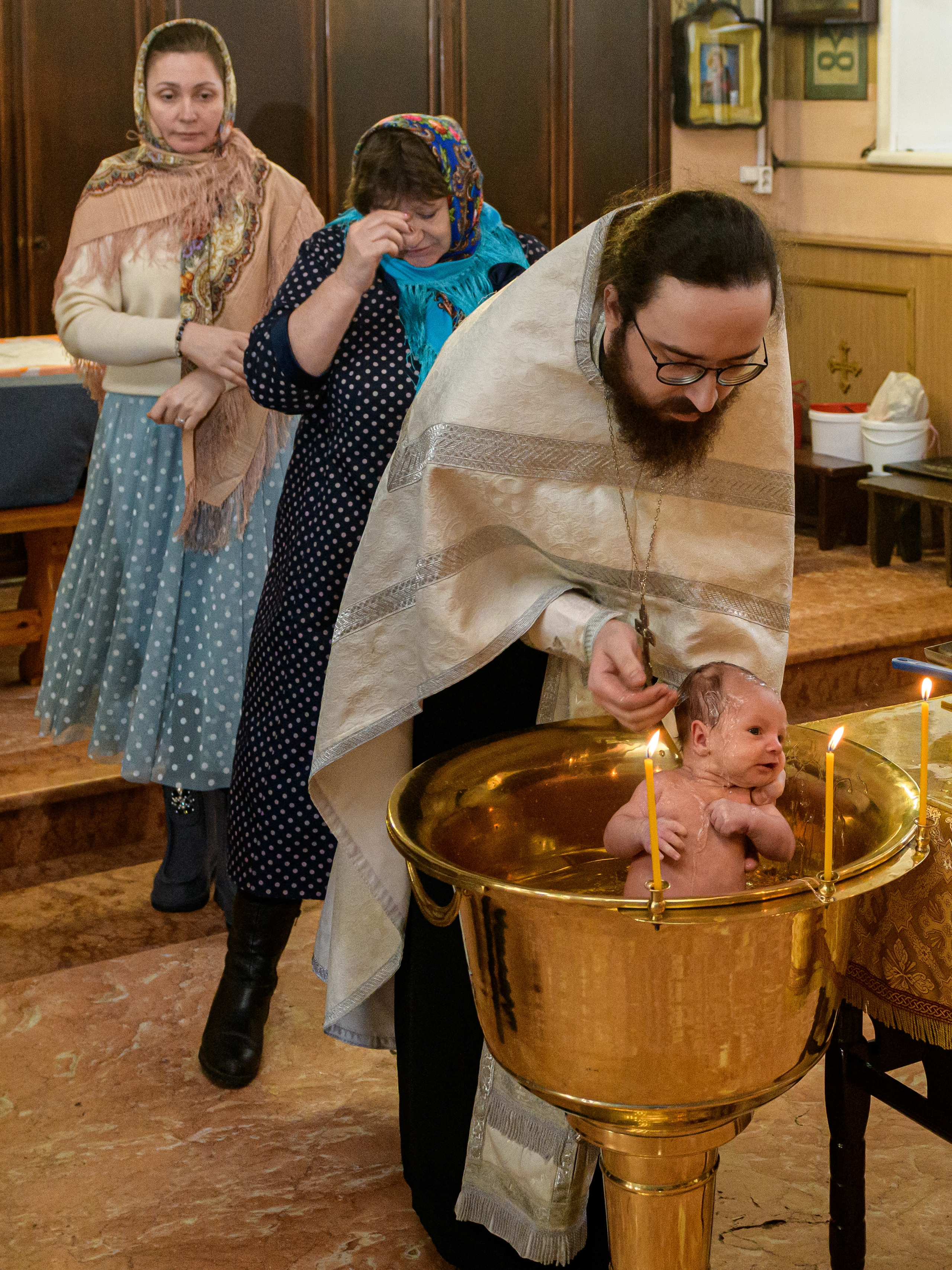 Крестины в церкви. Священник крестит маленького ребенка в купели во время таинства крещения в церкви