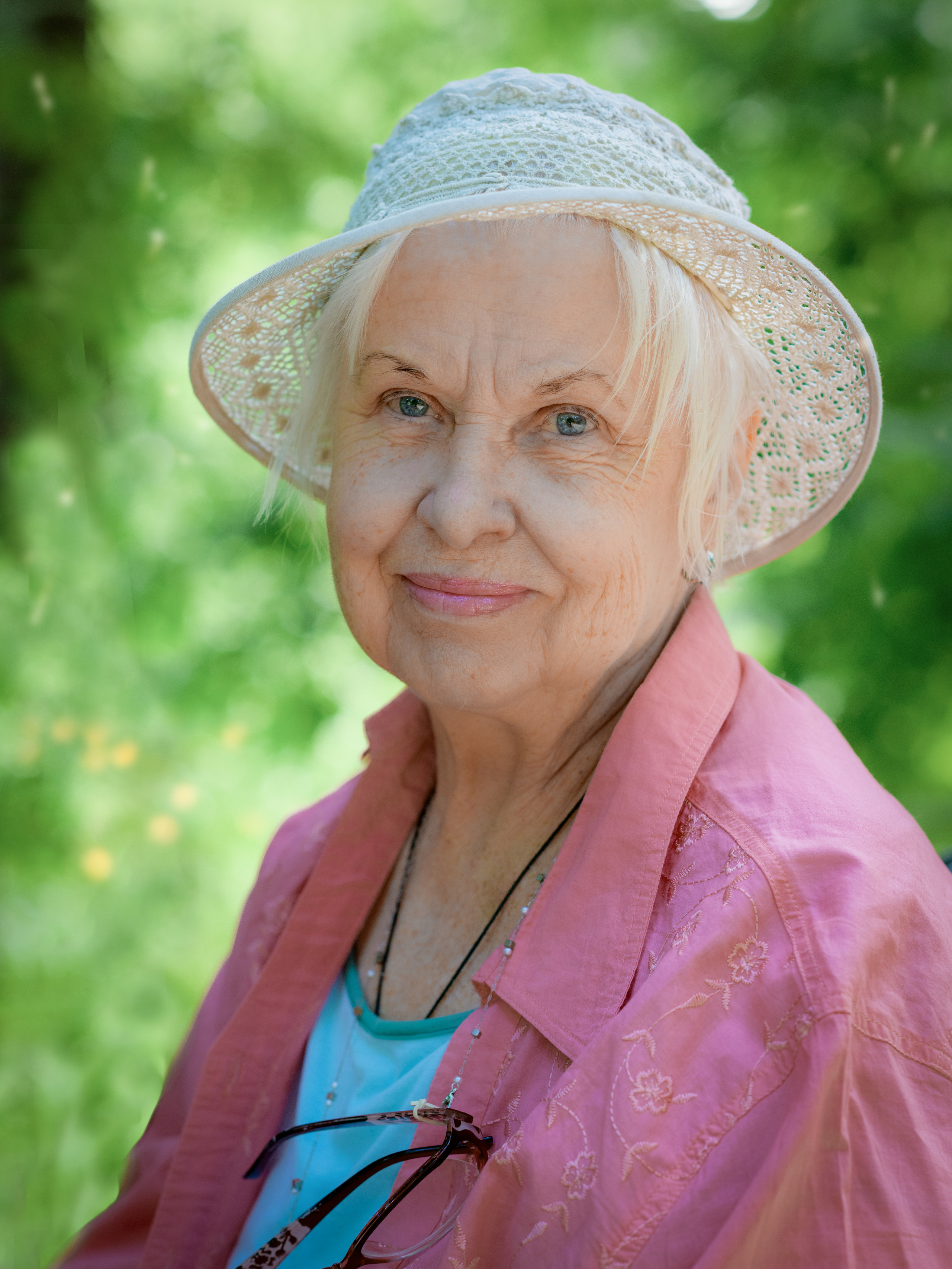 Женщина в преклонном возрасте в летней шляпке и красной куртке в парке летом