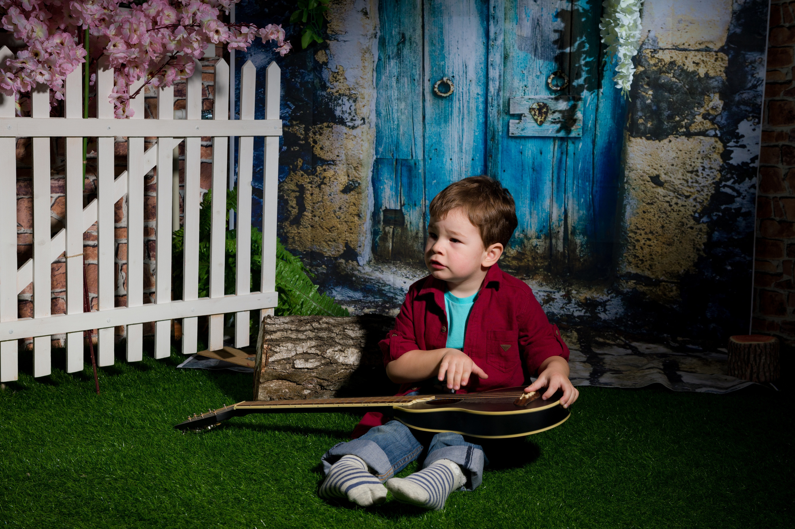 мальчик с гитарой сидит на траве на против двери и смотрит в сторону белого заборчика