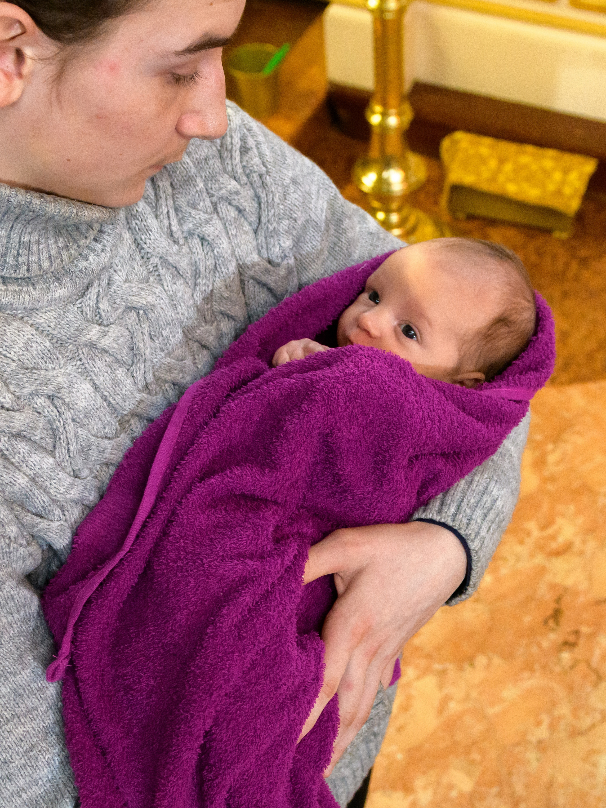 Крестины в церкви. молодой крестный держит крестника на руках и смотрит на него