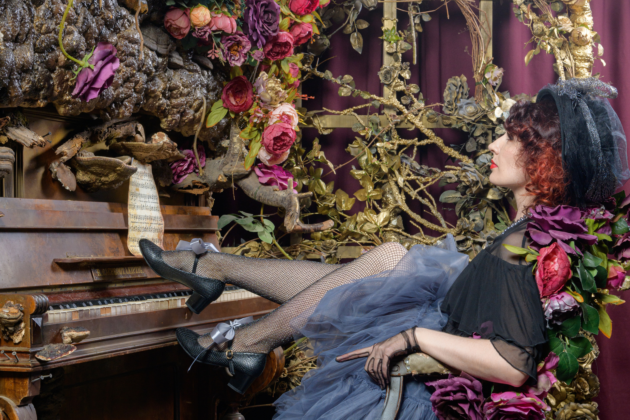 девушка сидит у пианино в фотозоне с цветами положив ноги на клавиши инструмента