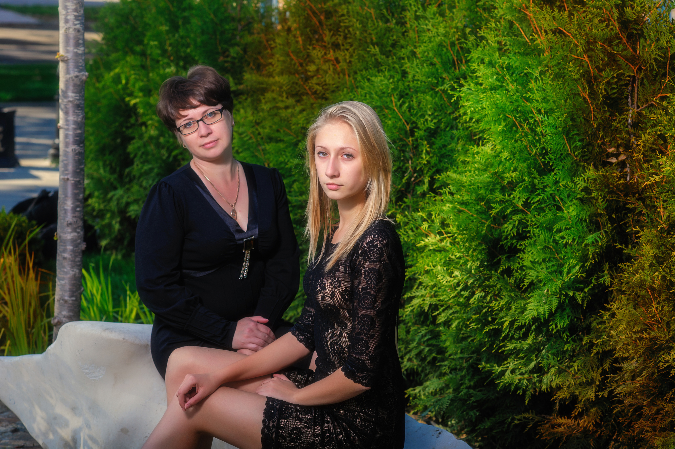 Дочка и мама сидят в парке на фоне зеленых растений