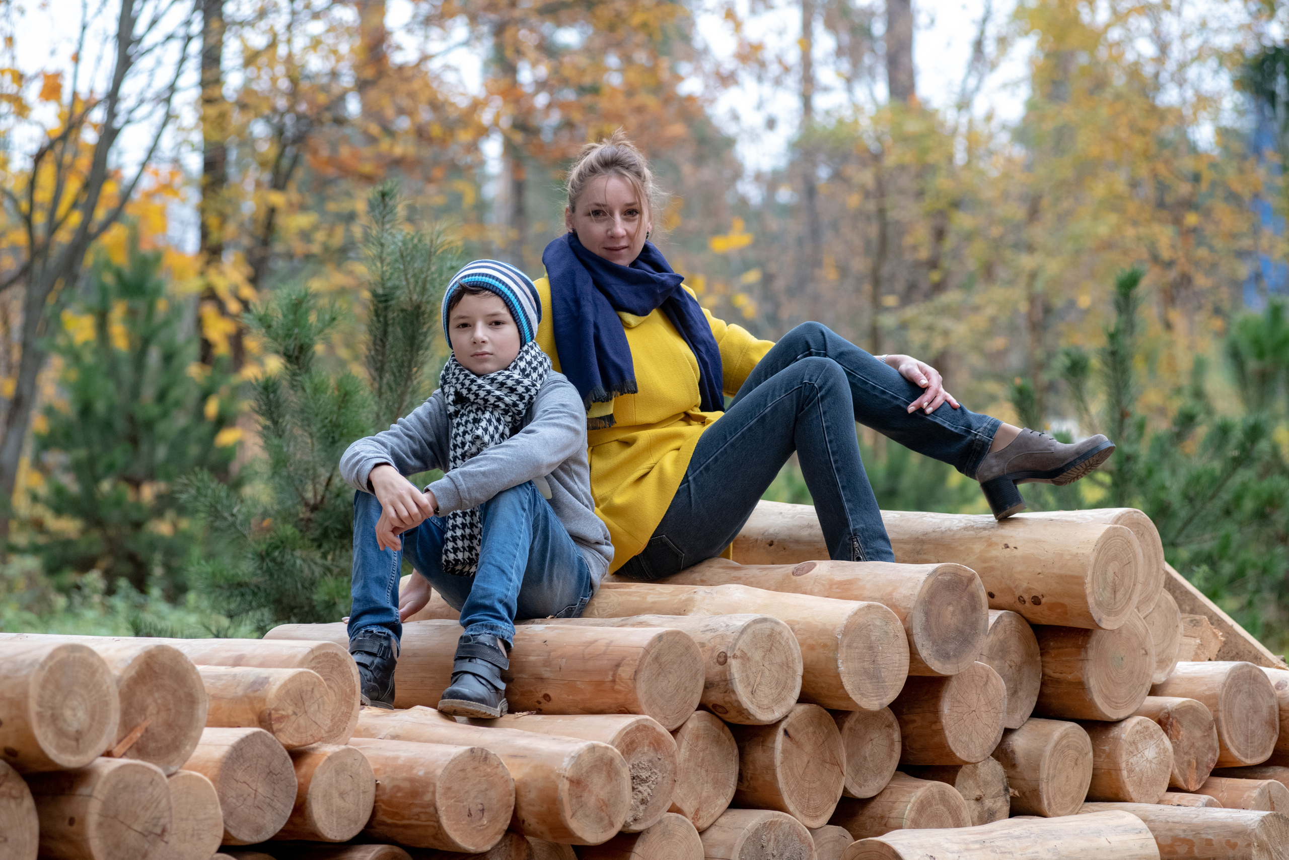 молодая женщина с сыном сидят на бревнах в лесу