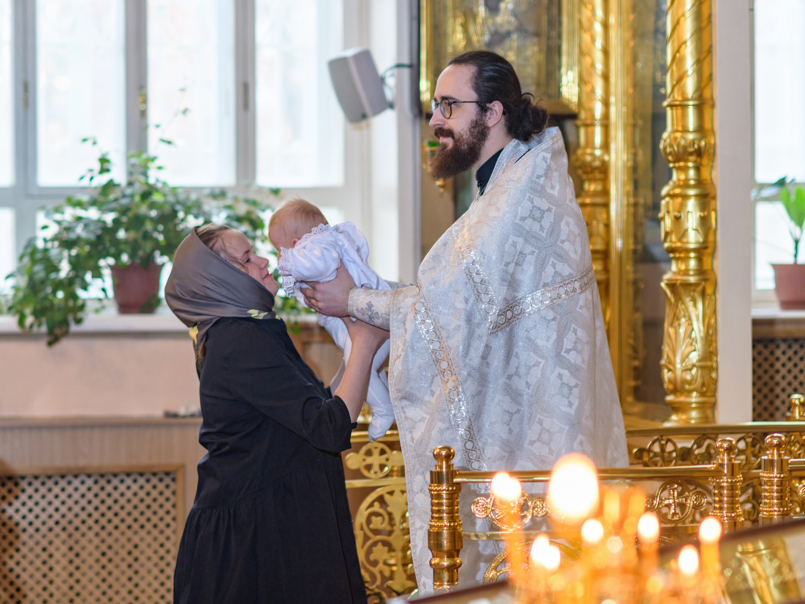 Крестины в церкви. священник передает ребенка маме после воцерковления после  обряда таинства крещения