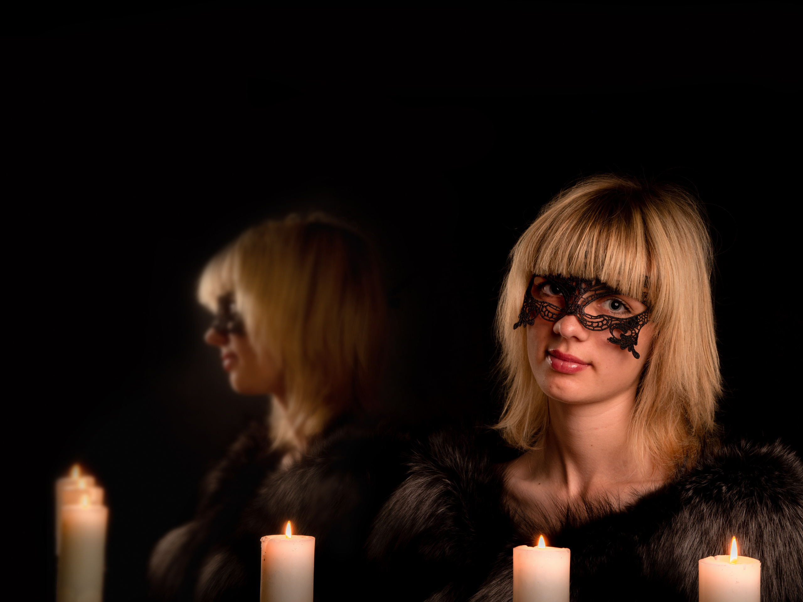 Девушка в кружевной черной маске сидит на против горящих свечей а сбоку ее отражение в зеркале