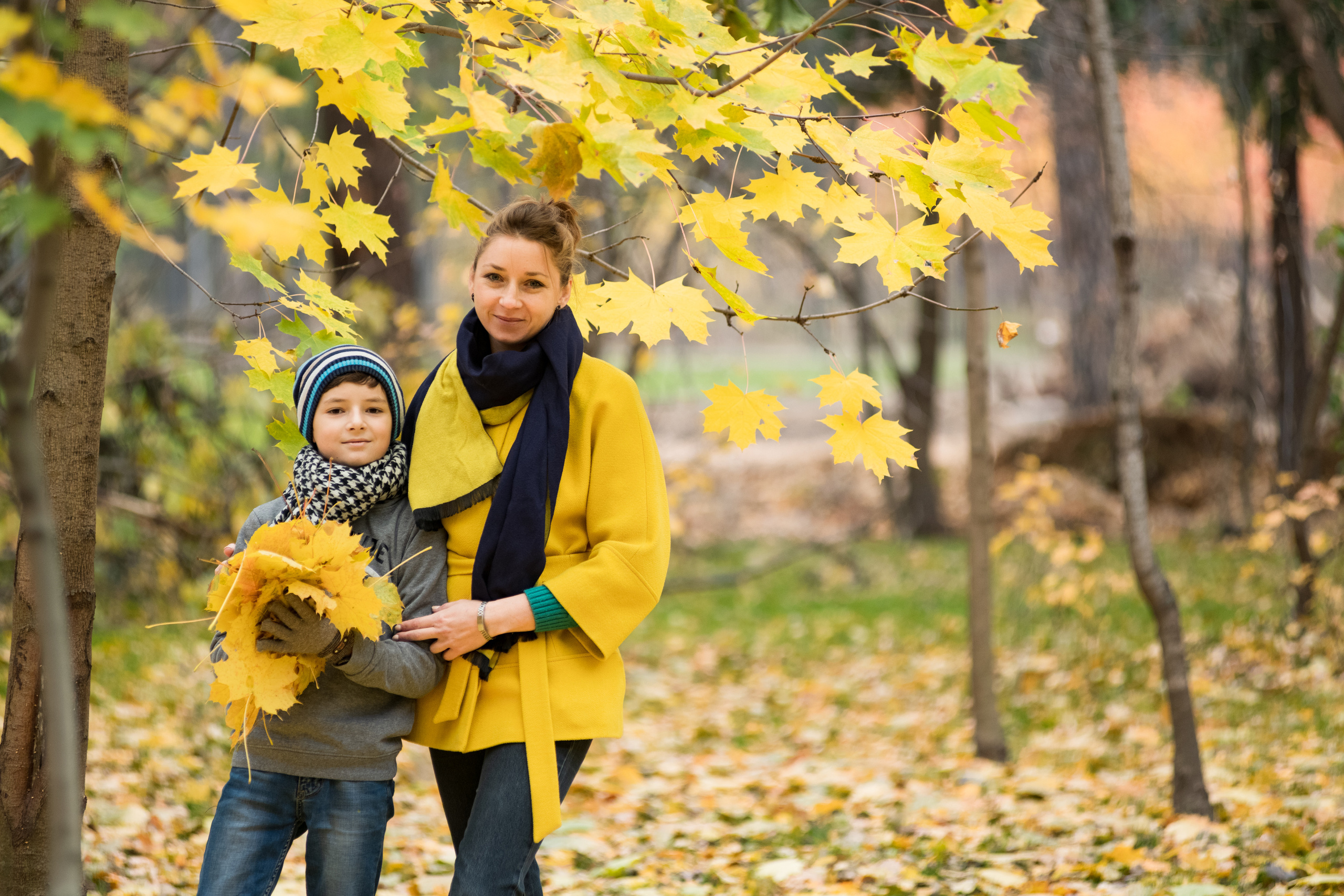 осенний парк и мама в желтом пальто с сыном держащим букет из кленовых листьев