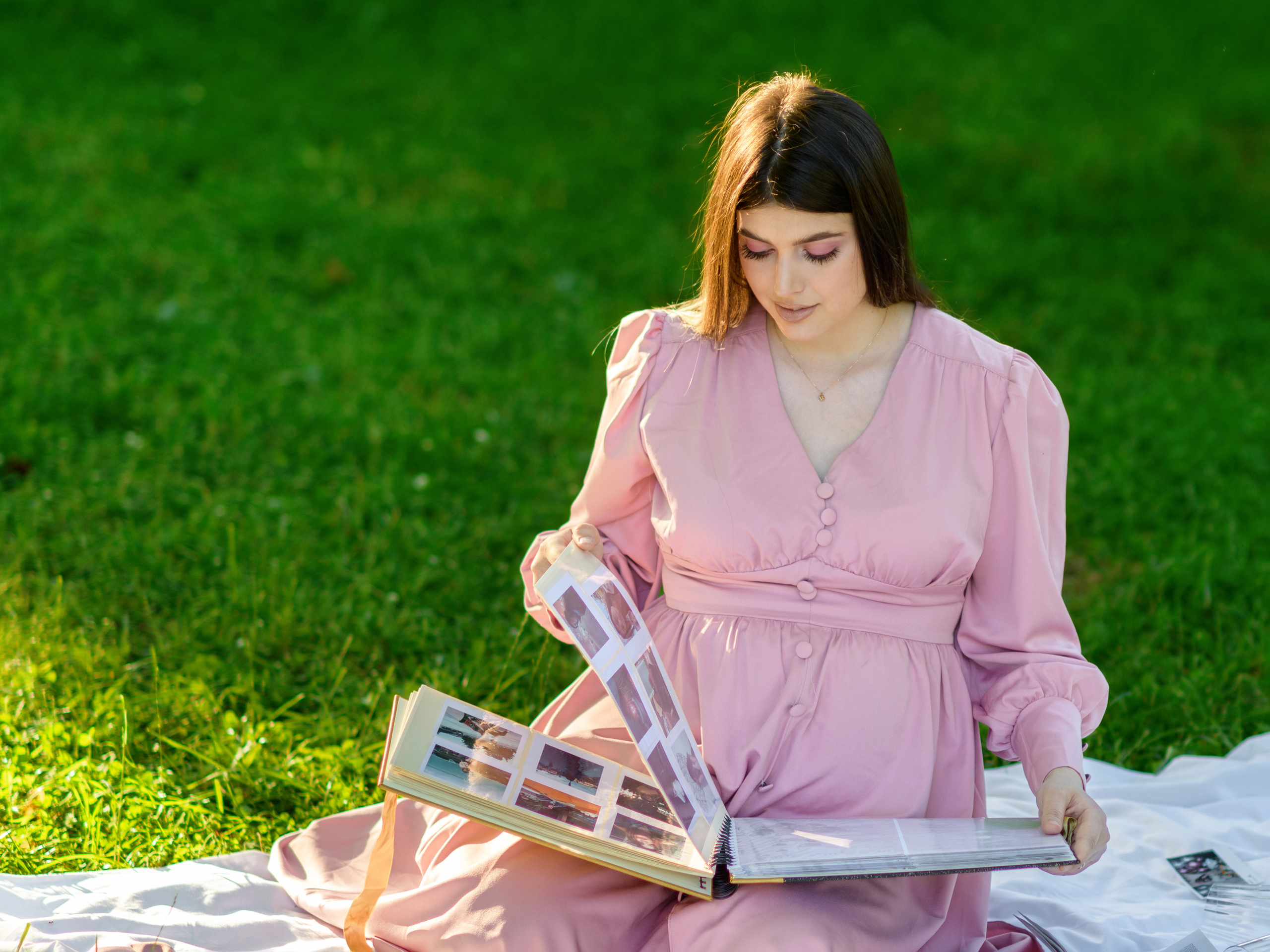 беременная девушка сидит в парке и разглядывает альбом с фотографиями