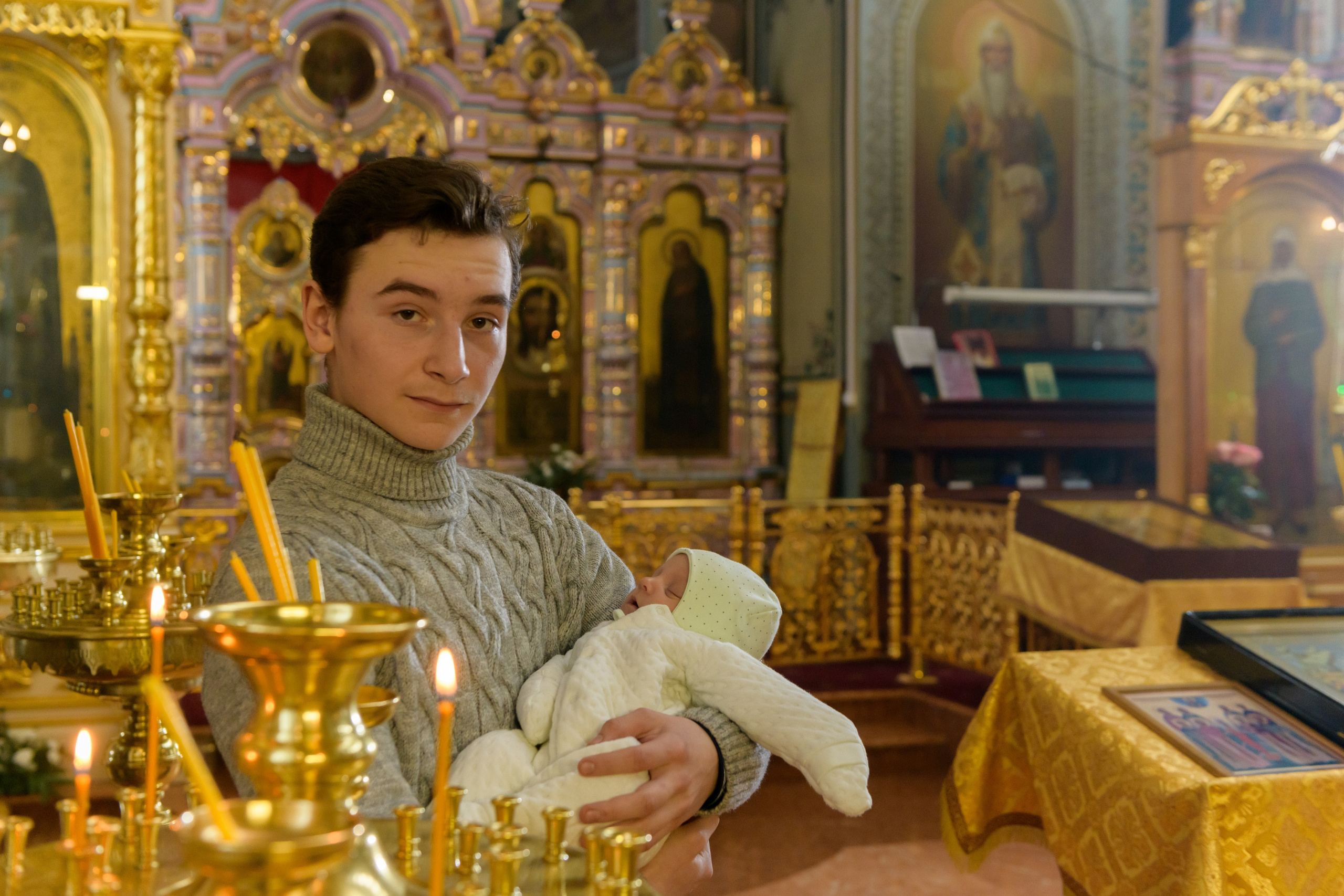 Крестины в церкви. молодой крестный с крестником на руках стоит у подсвечника в церкви