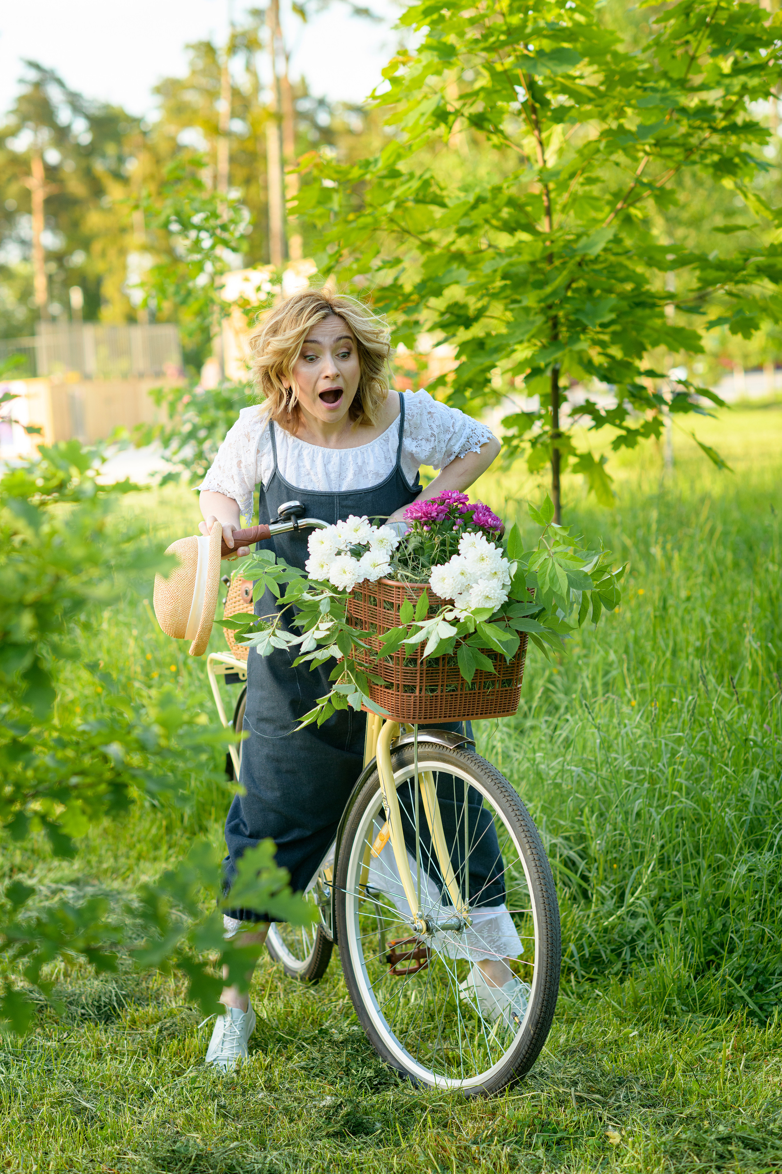 девушка в парке на велосипеде с огромным букетом цветов в корзине прикрепленной к рулю велосипеда