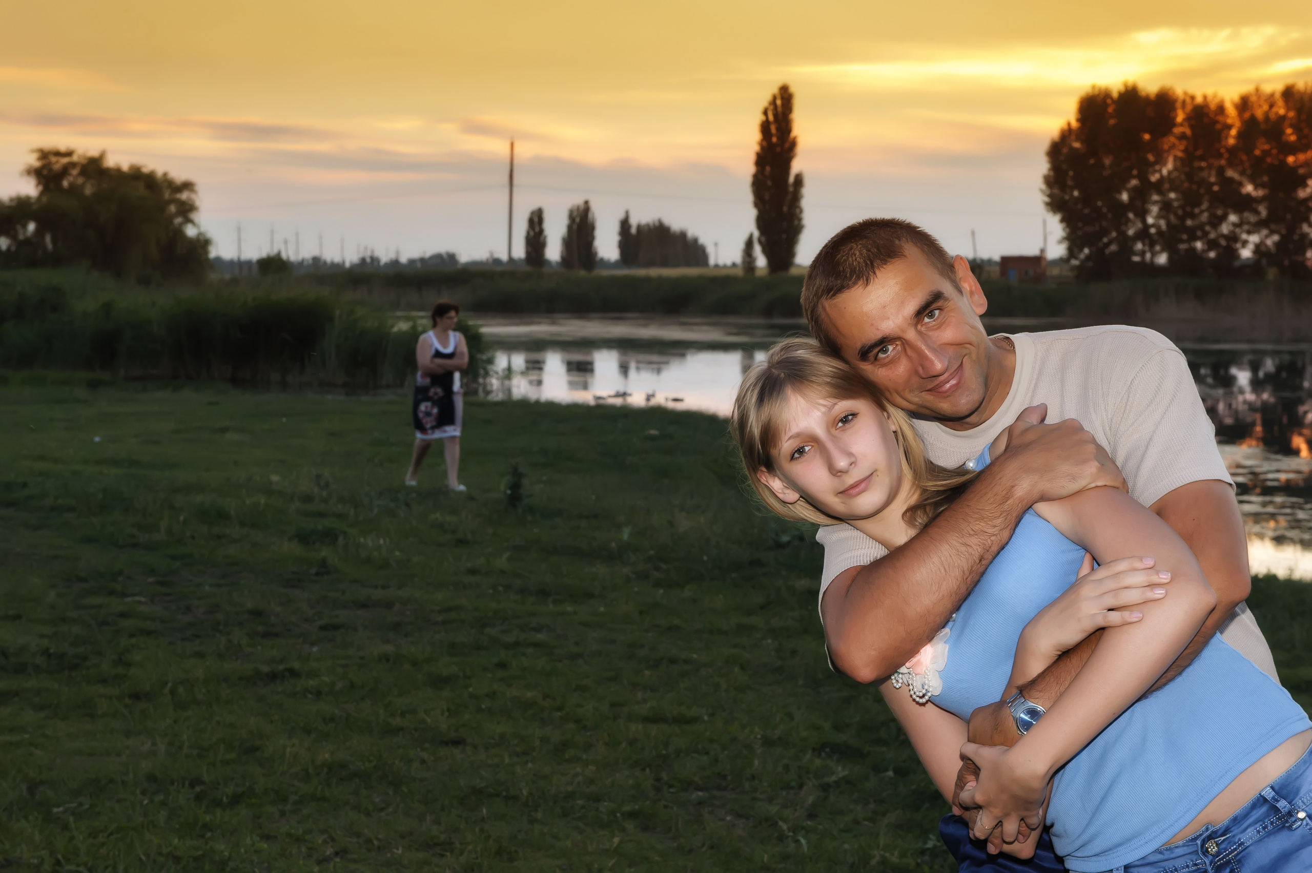 отец обнимает дочь на фоне заката и озера