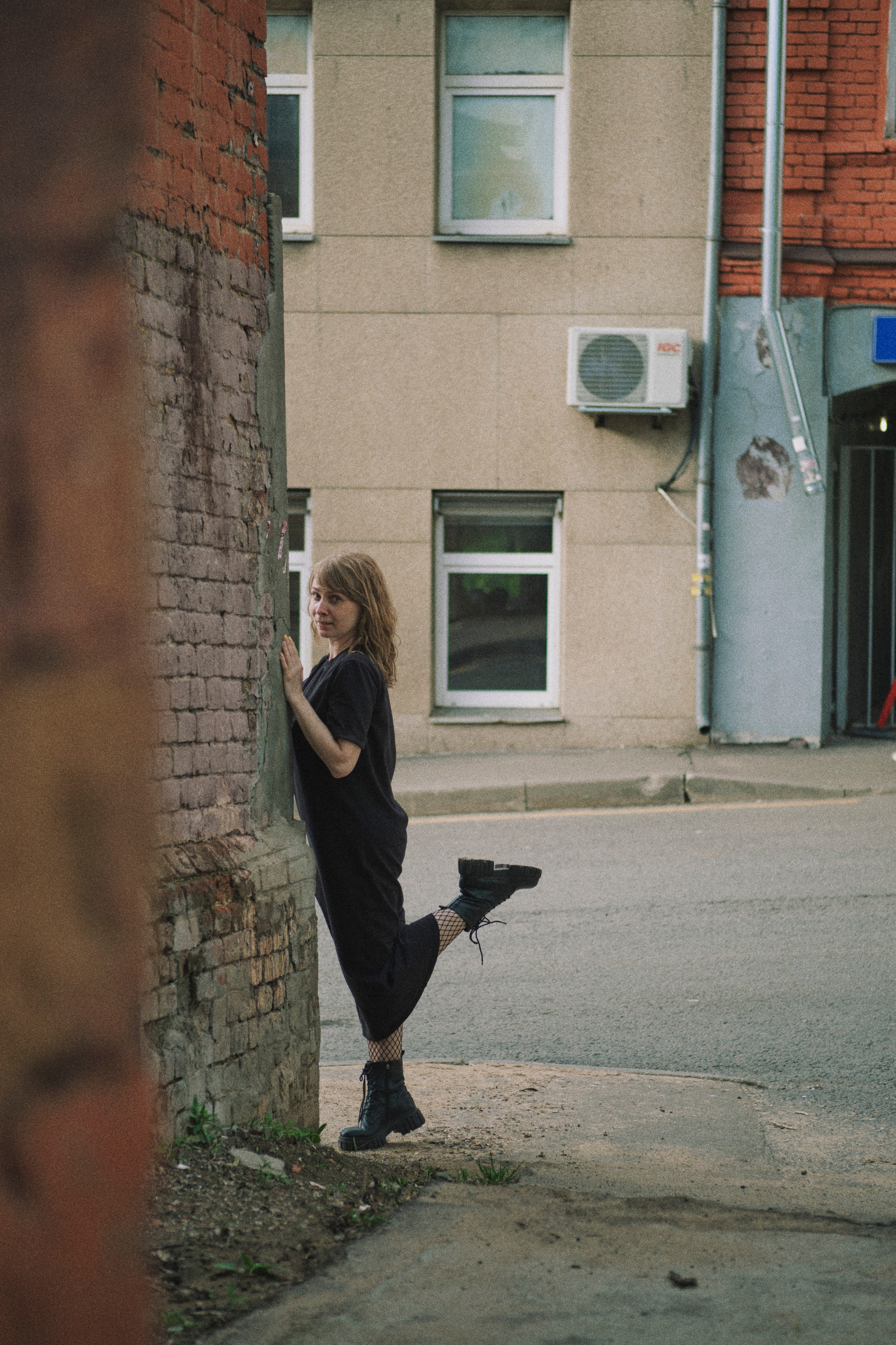 Женщина на улочках города стоит у угла дома, подняв одну ногу